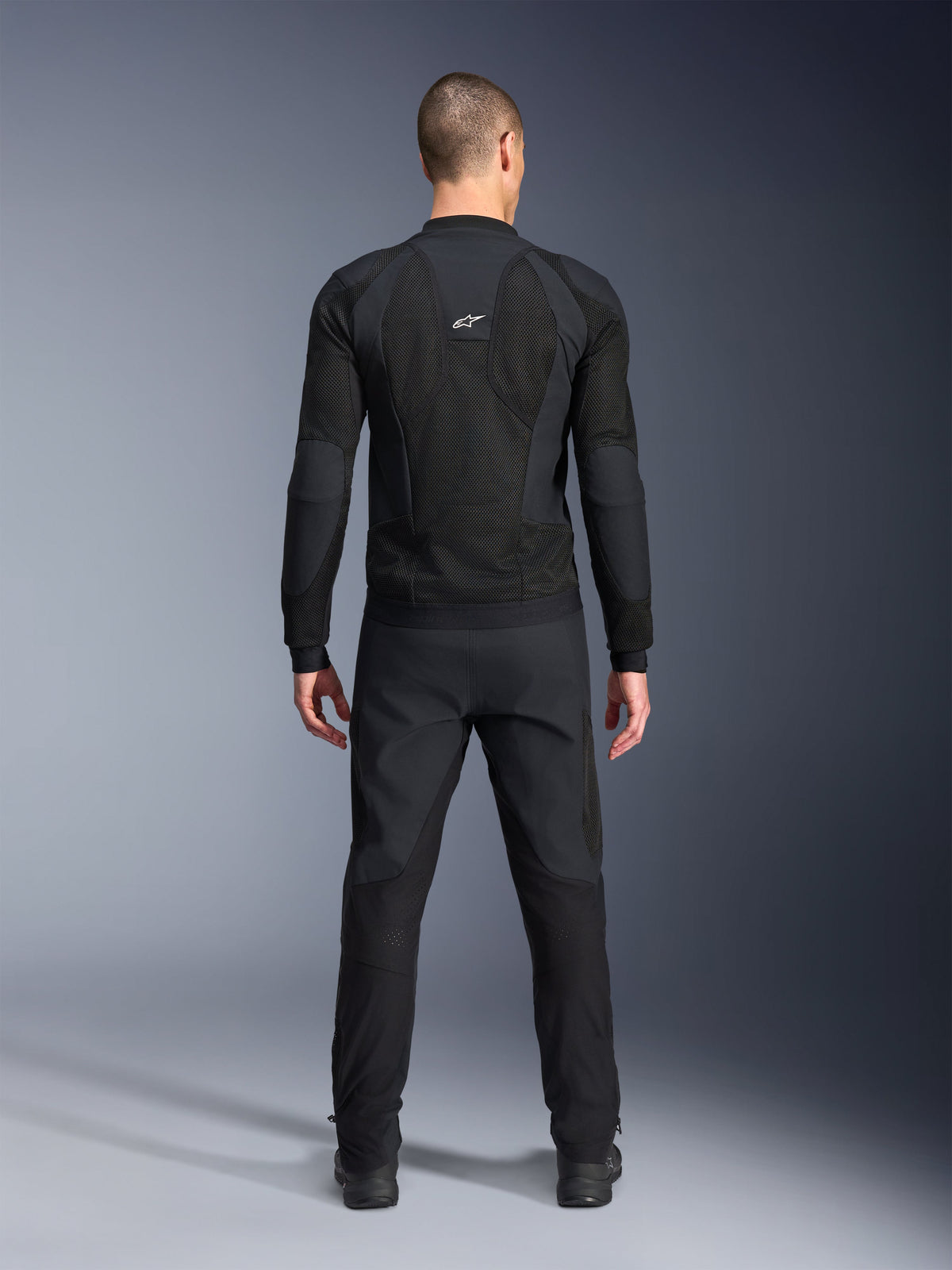Alpinestars Troop-Air Pro Jacke, Rückansicht, Schwarz, technische Motorrad-Air-Jacke mit großen Mesh-Belüftungspaneelen und weißem Alpinestars-Logo, kombiniert mit schwarzer Hose, urbane zeitgenössische Fahrausrüstung