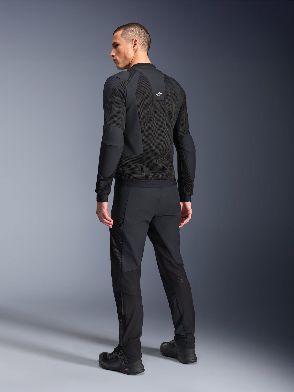 Alpinestars Troop-Air Pro Jacke, Schwarz, technische gepanzerte Mesh-Jacke in der Rückansicht, mit großflächigen Mesh-Einsätzen für optimale Luftzirkulation, kombiniert mit passender schwarzer technischer Hose und Schuhen.