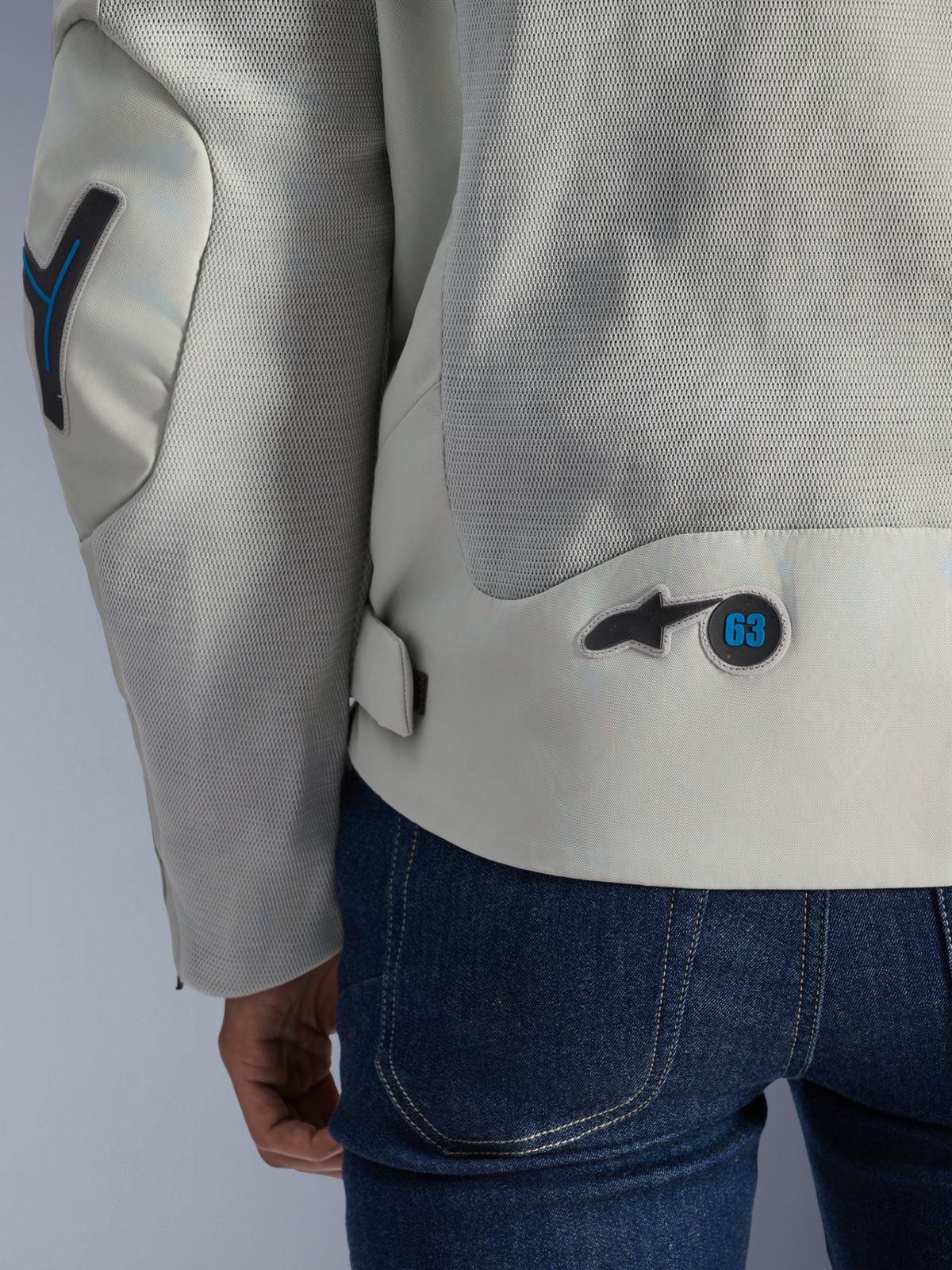 Alpinestars Circal-1 Air Jacke in Metal Gray mit Methyl Blue Akzenten, detaillierte Rückansicht mit recycelten Mesh-Luftstrom-Einsätzen und kreisförmigem '63'-Logo-Badge, getragen mit einer blauen Jeans.