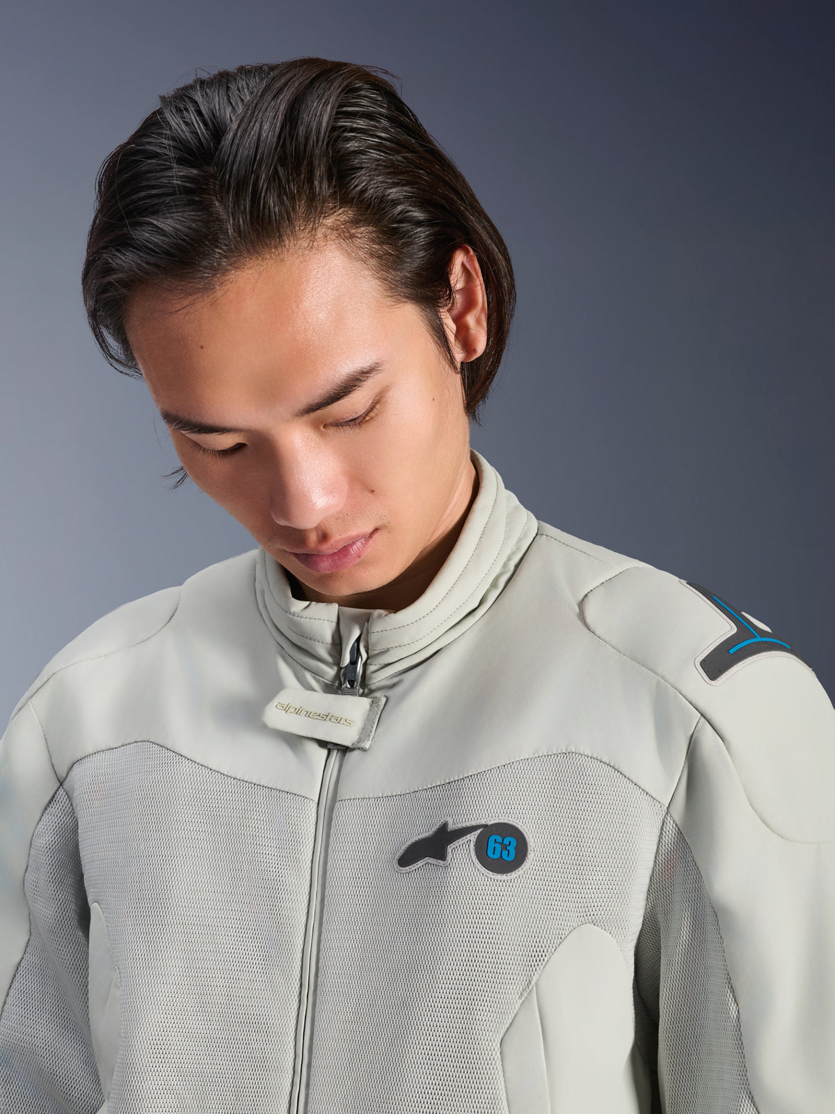 Männliches Model trägt die Alpinestars Circal-1 Air Jacke in Metal Gray mit Methyl Blue Akzenten, Nahaufnahme mit Fokus auf den Kragen, Mesh-Einsätze im Brustbereich und minimalistisches Logo-Branding, nachhaltige urbane Motorradausrüstung.
