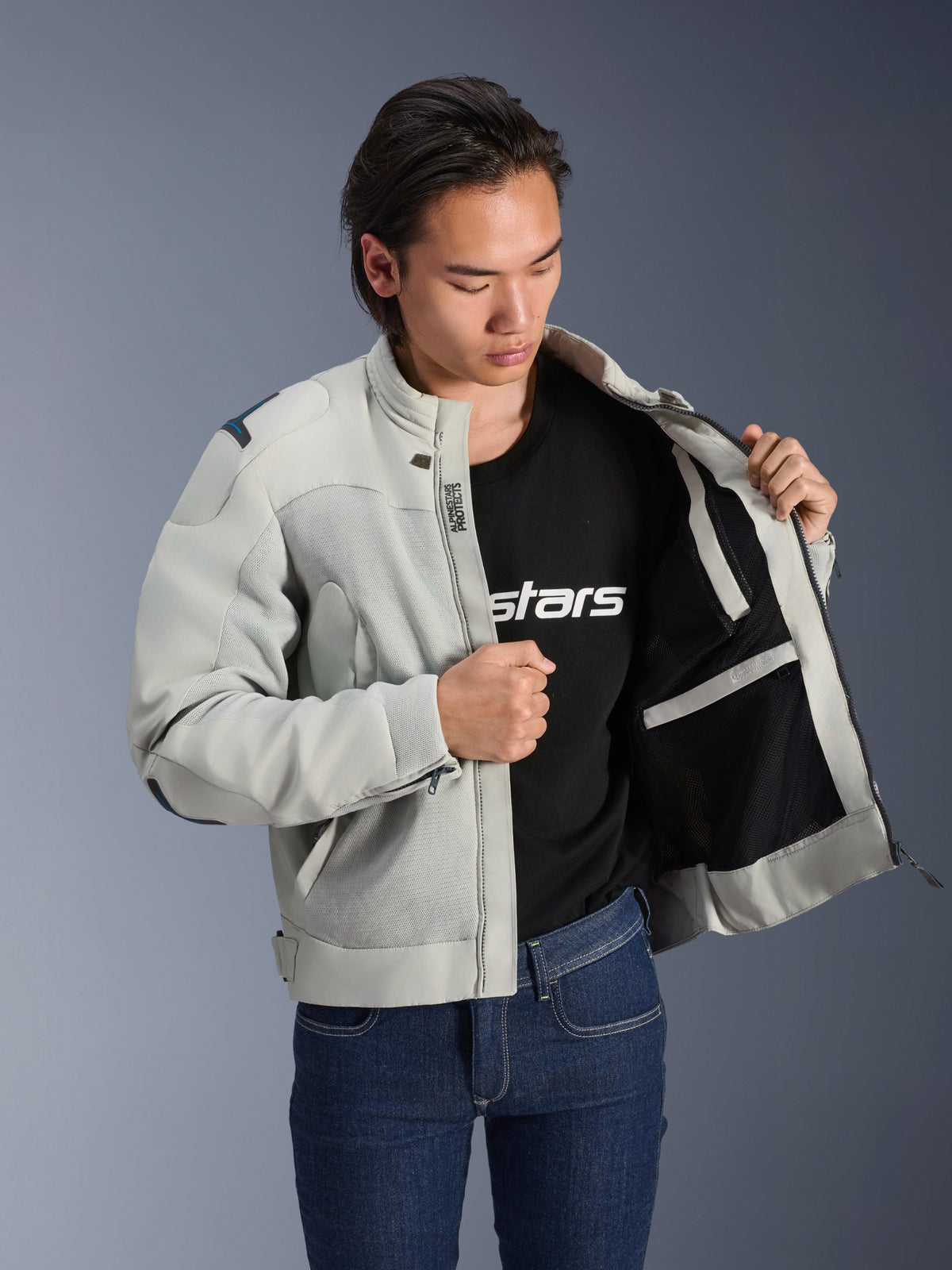 Alpinestars Circal-1 Air Jacke, Metal-Grau, offen gehalten, um das Mesh-Innenfutter und die Taschendetails zu zeigen, getragen von einem Model mit schwarzem Logo-T-Shirt und blauen Jeans, urbaner Motorrad-Stil