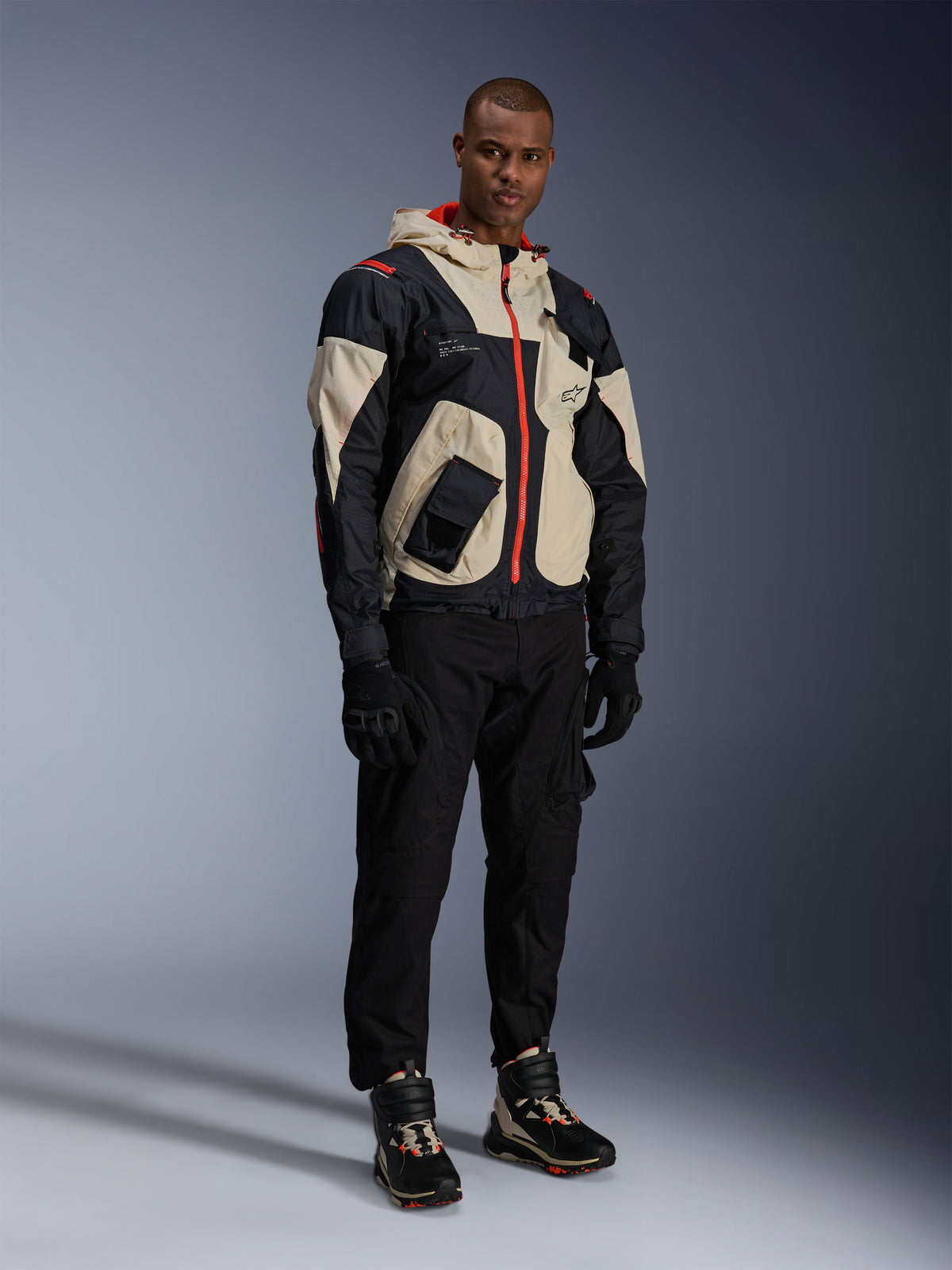 Man in volledige urban motoruitrusting, met Alpinestars Speedstreet schoenen in Black Almond Hot Orange en een Mogress Air Jacket in zwart en crème, gecombineerd met een zwarte broek en handschoenen, streetwear-geïnspireerde beschermende outfit voor stadsritten