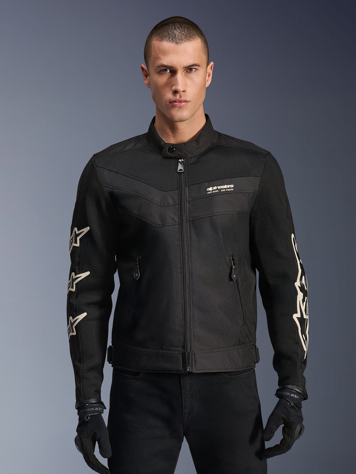 Alpinestars T-Dyno Air Jacke, schwarze Textil-Motorradjacke, mit weißen Sterngrafiken auf den Ärmeln und Logo auf der Brust, Mesh-Einsätzen zur Belüftung, Vintage-inspirierter Biker-Passform, getragen mit schwarzen Handschuhen und Hose