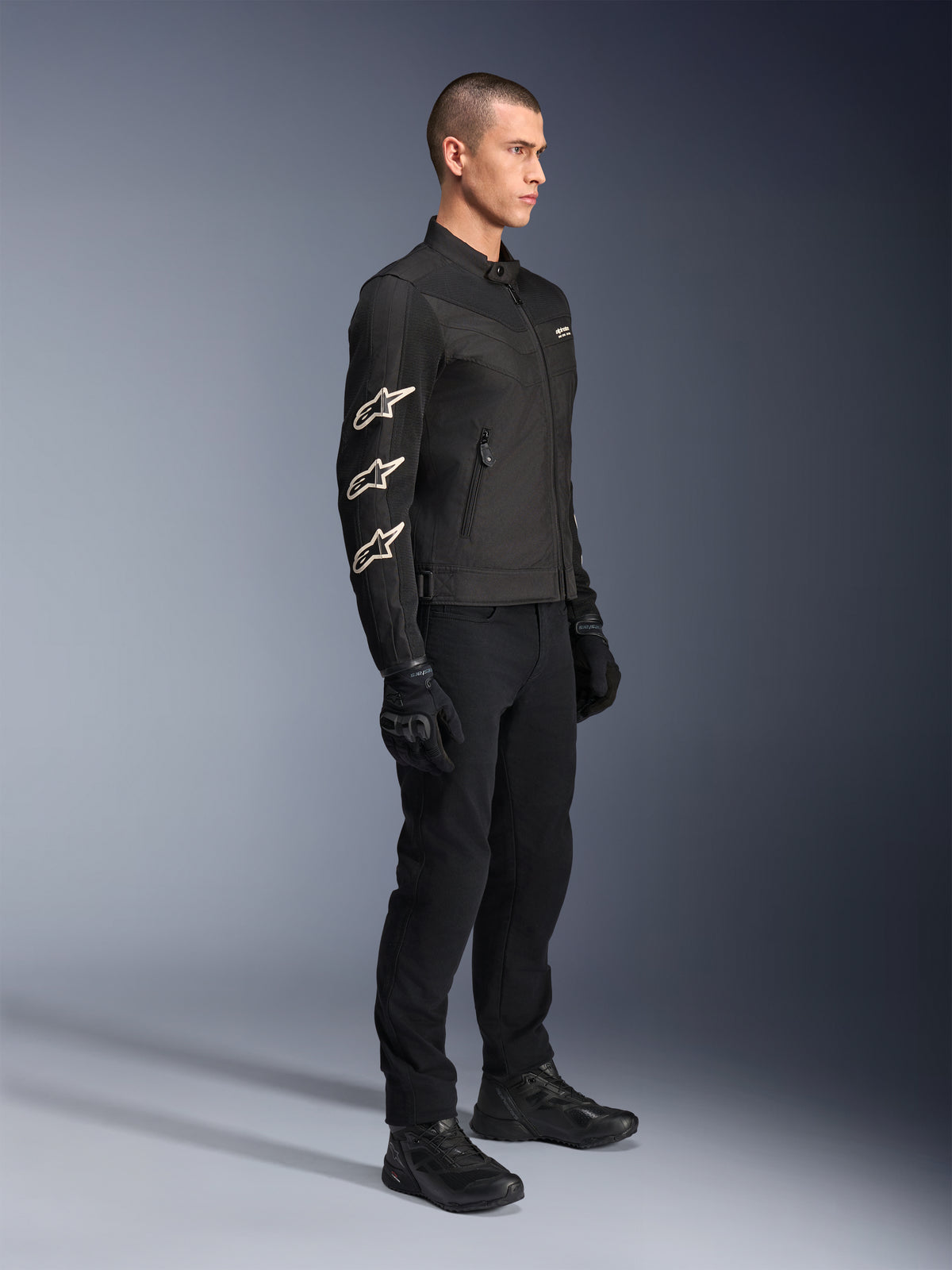 Alpinestars T-Dyno Air Jacke, Schwarz, Motorrad-Textiljacke, mit drei weißen Alpinestars-Logos auf dem Ärmel, getragen mit passender schwarzer Hose und Handschuhen, urbane Fahrausrüstung mit atmungsaktiven Mesh-Paneelen