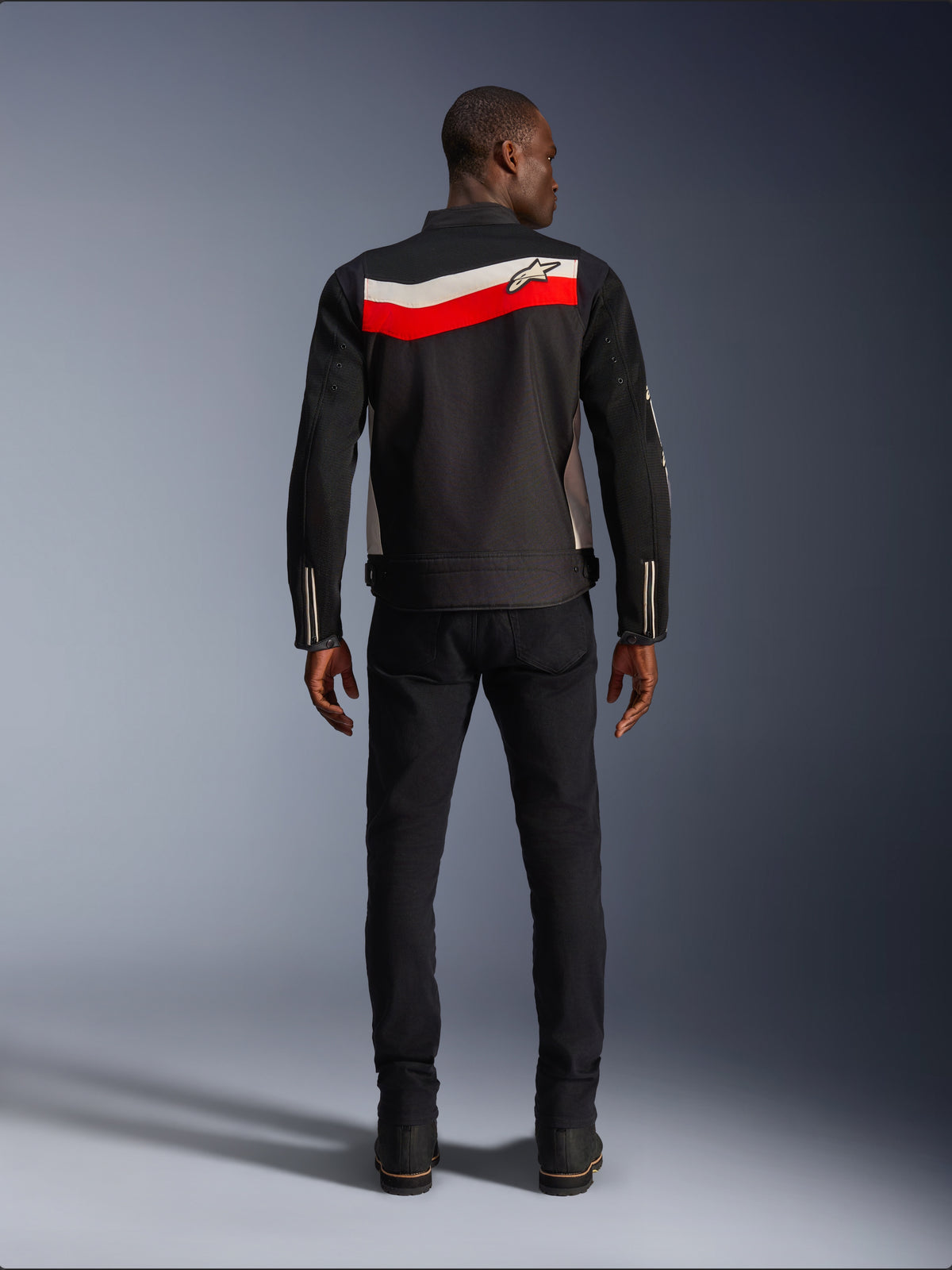 Alpinestars T-Dyno Air Jacke, Motorrad-Textiljacke für Herren, Rückansicht, Schwarz mit leuchtend roten und ecrufarbenen horizontalen Streifen auf dem Rücken, Alpinestars-Logo auf der Passe, getragen mit schwarzer Hose und Stiefeln, atmungsaktive 3D-Mesh-Konstruktion