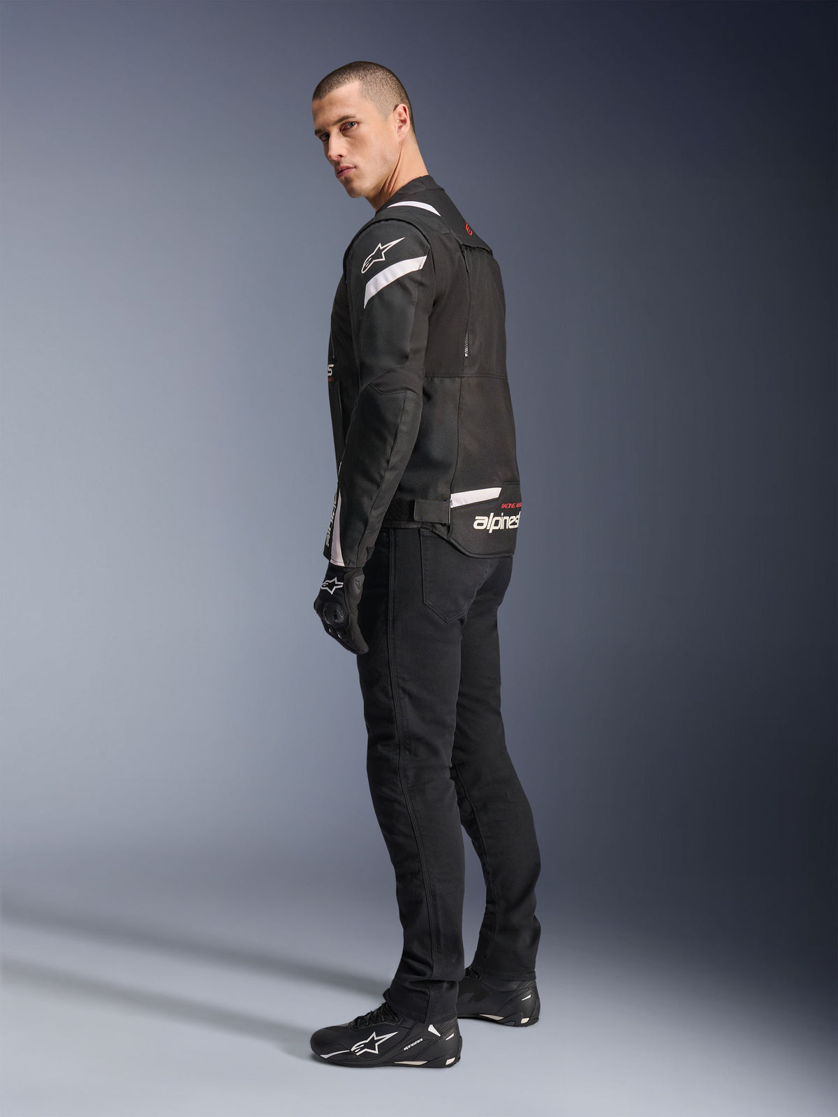 Alpinestars T-Stunt Air Jacket, Black and White, modular motorcycle jacket with tech mesh panels, shown from a back-side profile on a model, worn with black riding pants and shoes, featuring white accents and branding on the shoulders and back.