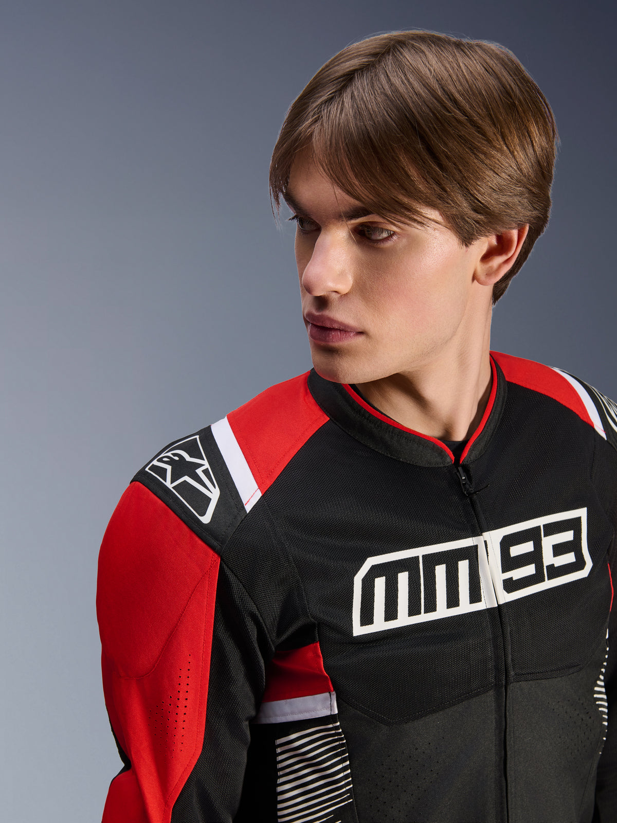 Männliches Modell trägt Alpinestars MM93 T-SPS Air V2 Jacke, Textil-Motorradjacke, Schwarz, Leuchtendes Rot und Weiß, mit markantem MM 93-Branding auf der Brust und Stern-Logo auf der Schulter, Mesh-Konstruktion für Luftstrom, sportorientierte Fahrausrüstung