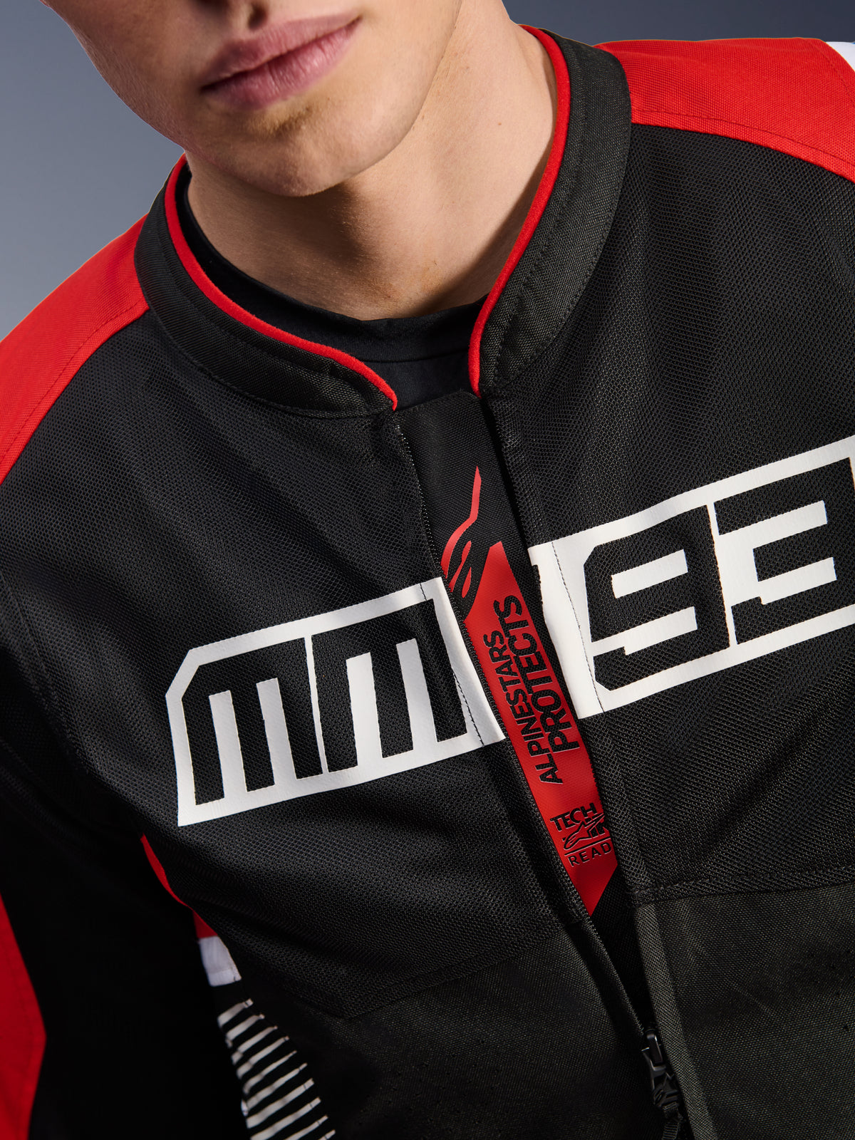 Alpinestars MM93 T-SPS Air V2 Jacke, Motorradjacke, Schwarz, Leuchtendes Rot und Weiß, Nahaufnahme des Brustbereichs mit großem weißen MM93-Logo, roter „Alpinestars Protects“- und „Tech-Air Ready“-Reißverschlusslasche, Tech-Mesh-Gewebestruktur