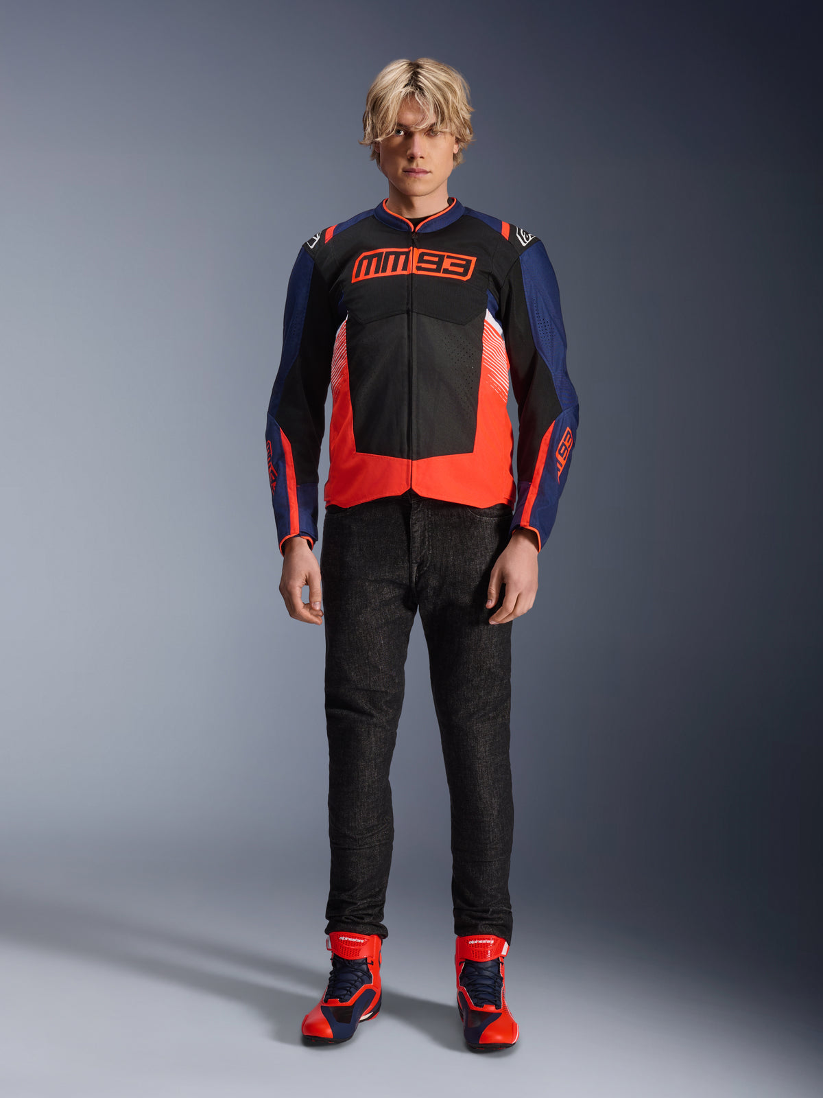 Alpinestars MM93 T-SPS Air V2 Jacke, Dunkelblau und Schwarz mit Red Fluo Akzenten, charakteristisches MM93-Logo auf der Brust, getragen mit schwarzer Motorradhose und passenden blau-roten Stiefeln, urbanes Motorrad-Outfit