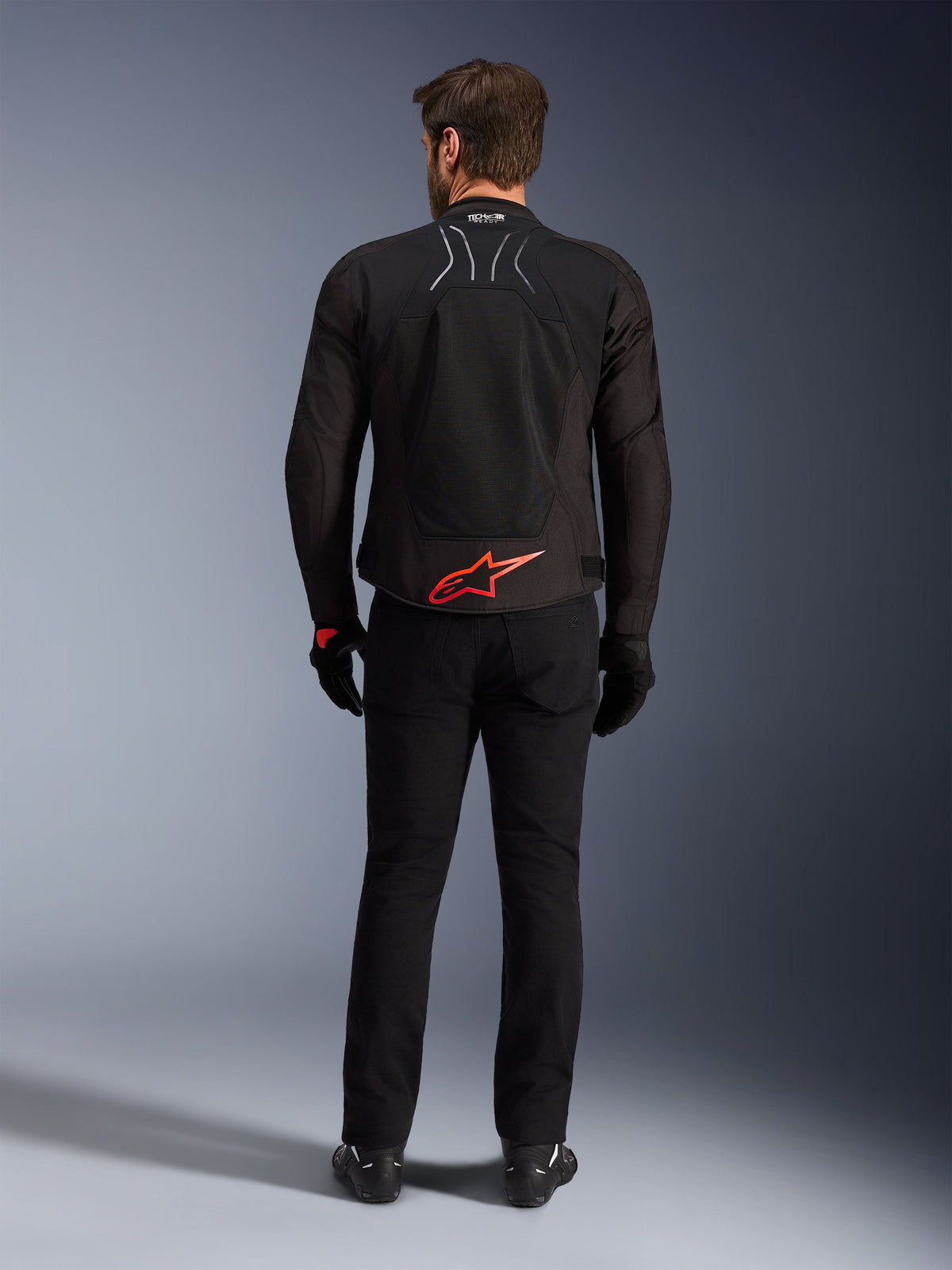 Veste Alpinestars SMX Air, noire avec logo rouge vif, vue arrière montrant le marquage Tech-Air Ready et les panneaux de ventilation en maille, portée avec un pantalon et des gants noirs, équipement de moto de sport et de course haute performance