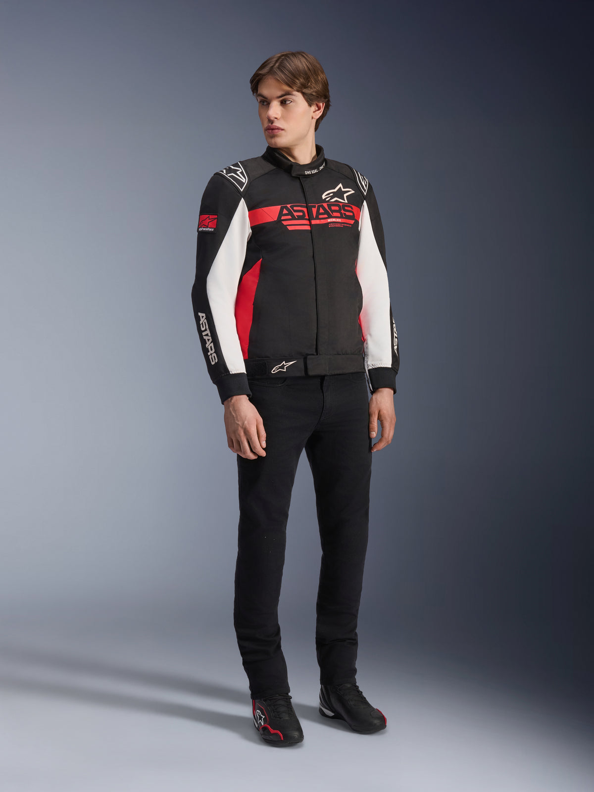 Veste Alpinestars Monza Sport, noir, rouge vif et blanc, veste de moto en textile, design inspiré de la course avec logo ASTARS sur la poitrine et les manches, portée par un mannequin avec un pantalon noir et des chaussures de moto, équipement de conduite sport décontracté