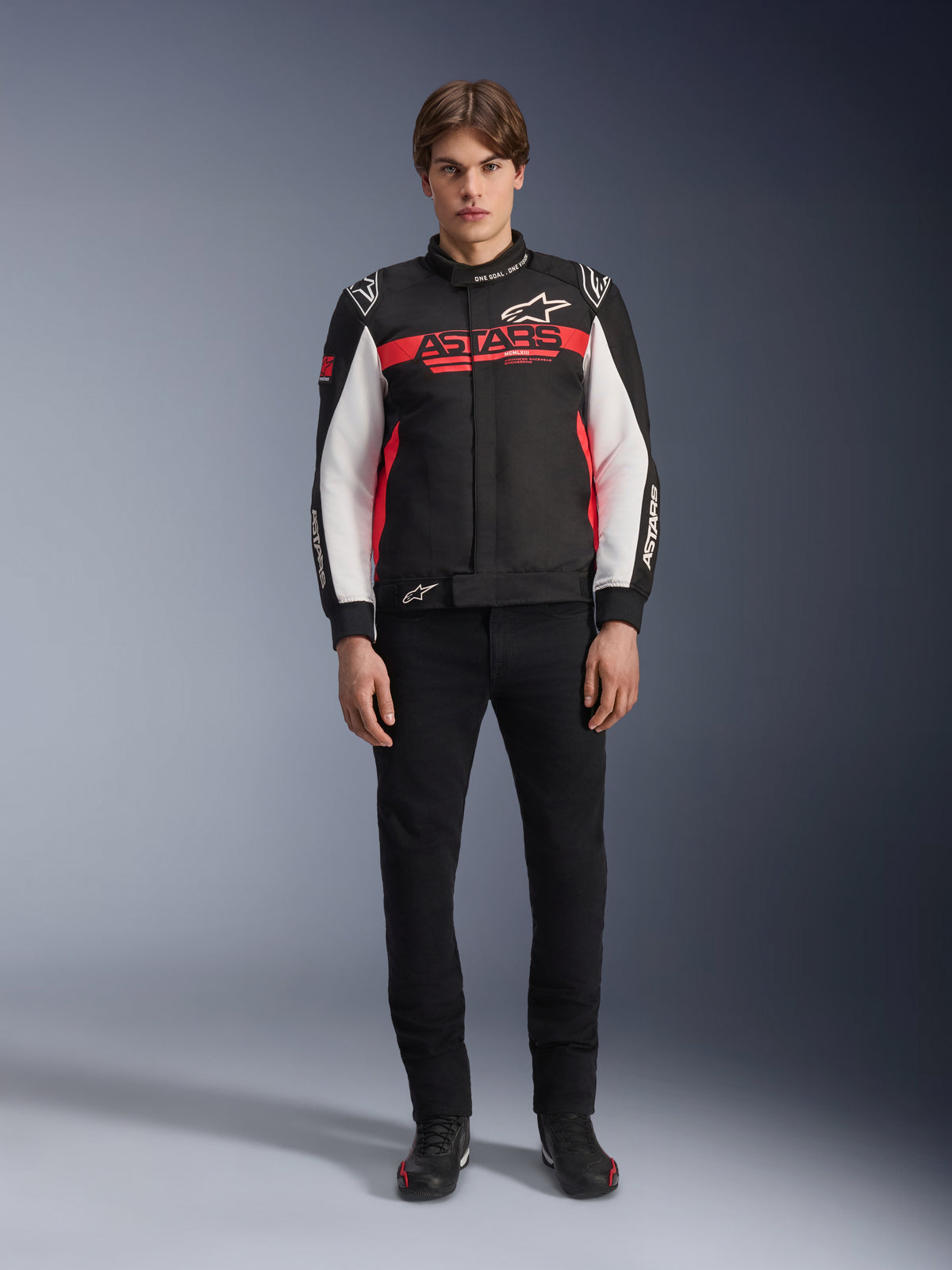 Mannequin homme portant la veste Alpinestars Monza Sport en noir, rouge vif et blanc, arborant un large logo 'ASTARS' rouge sur la poitrine et des empiècements blancs sur les manches, associée à un pantalon noir et des bottes de moto noires.