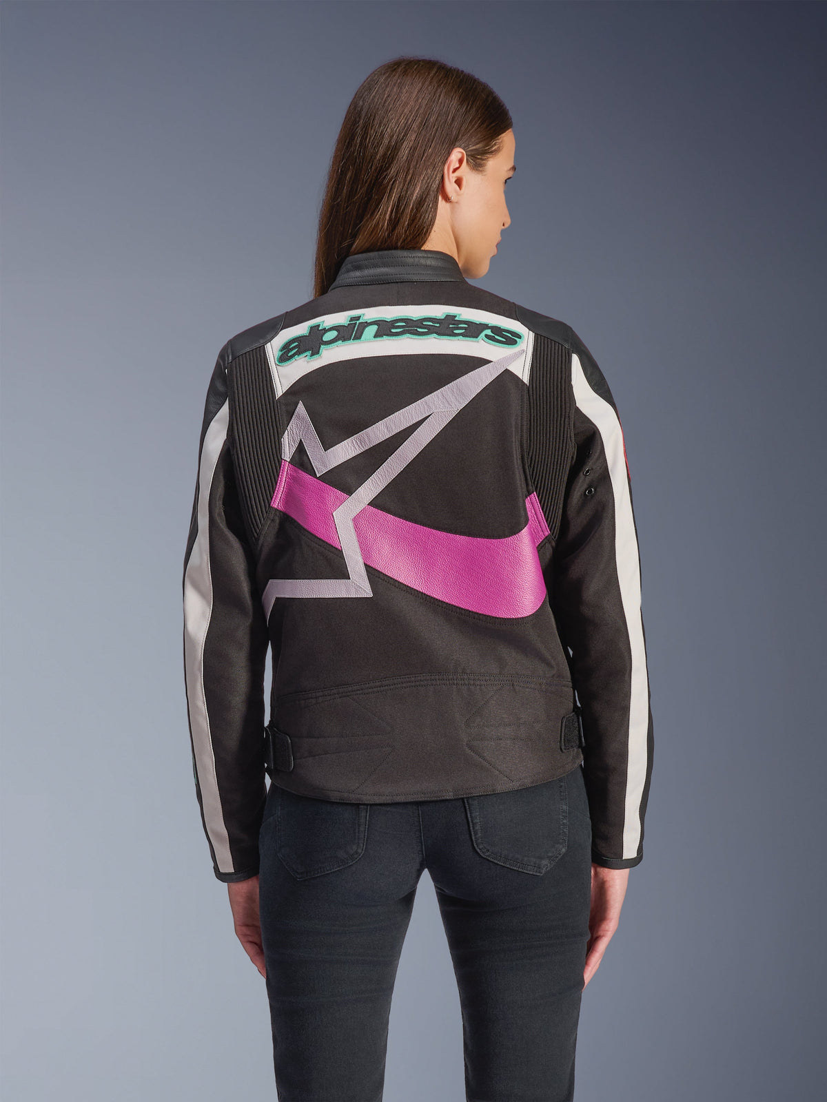 Alpinestars Idles Damenjacke, Rückansicht, Schwarz, Off-White und Lila, großes grafisches Stern-Logo auf dem Rücken, petrolfarbener gestickter Schriftzug, Akkordeon-Einsätze an den Schultern, vintage-inspirierte urbane Motorradbekleidung