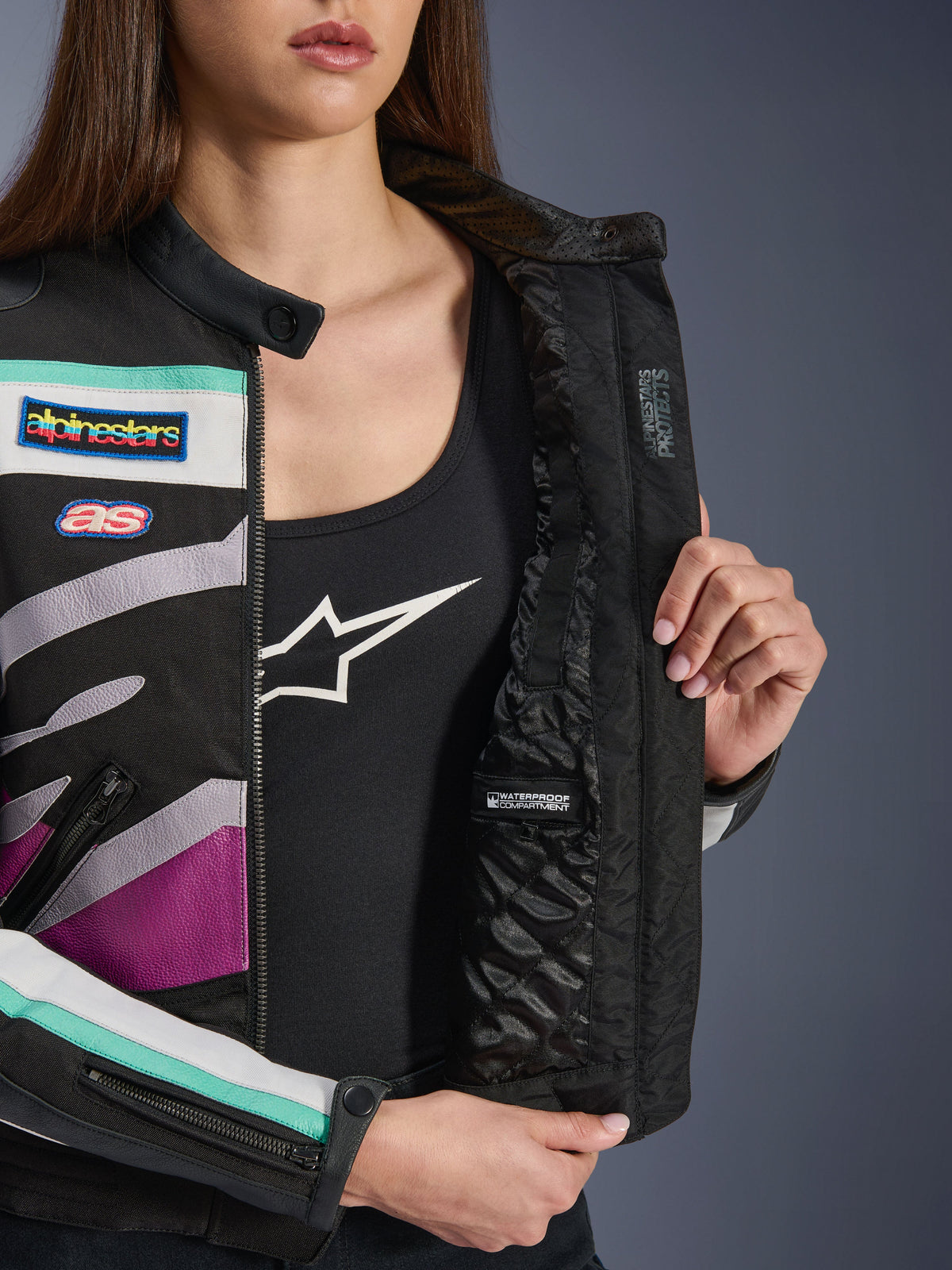 Alpinestars Idles Damenjacke, Schwarz, Off-White, Lila, Nahaufnahme des gesteppten Innenfutters mit wasserdichtem Fach, mit von Vintage-Rennsport inspirierten Aufnähern und farbenfrohen Akzenten in Petrol und Lila auf der Außenseite aus Textil.