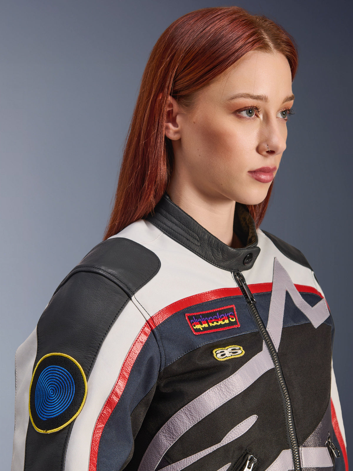 Alpinestars Idles Damenjacke, Off-White, Flame-Red und Schwarz, mit von Vintage-Rennsport inspirierten Aufnähern und einem umlaufenden Logo, Textil- und Lederkonstruktion, urbaner Motorrad-Stil, getragen von einem Modell.