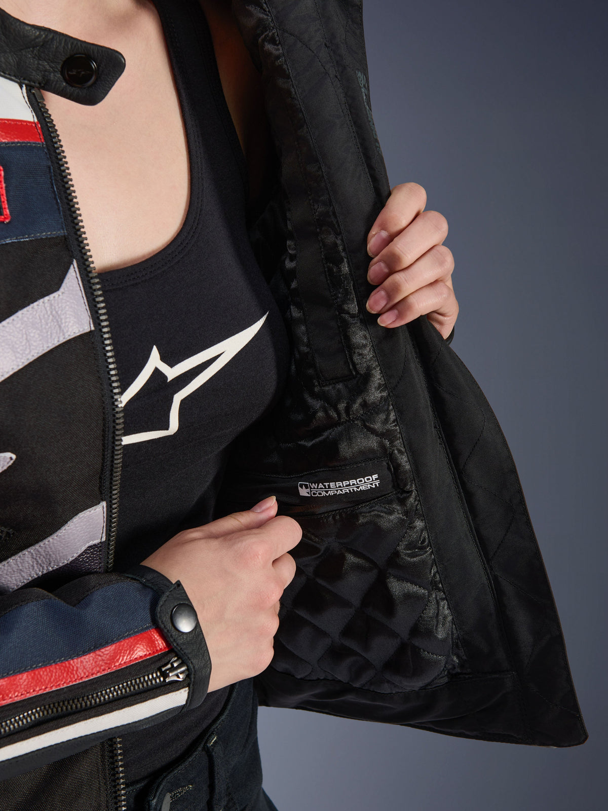 Alpinestars Idles Damenjacke, Innendetail mit schwarzem Steppfutter und gekennzeichnetem wasserdichtem Fach, getragen über einem schwarzen Tanktop mit Logo, funktionale Motorradbekleidung für Damen