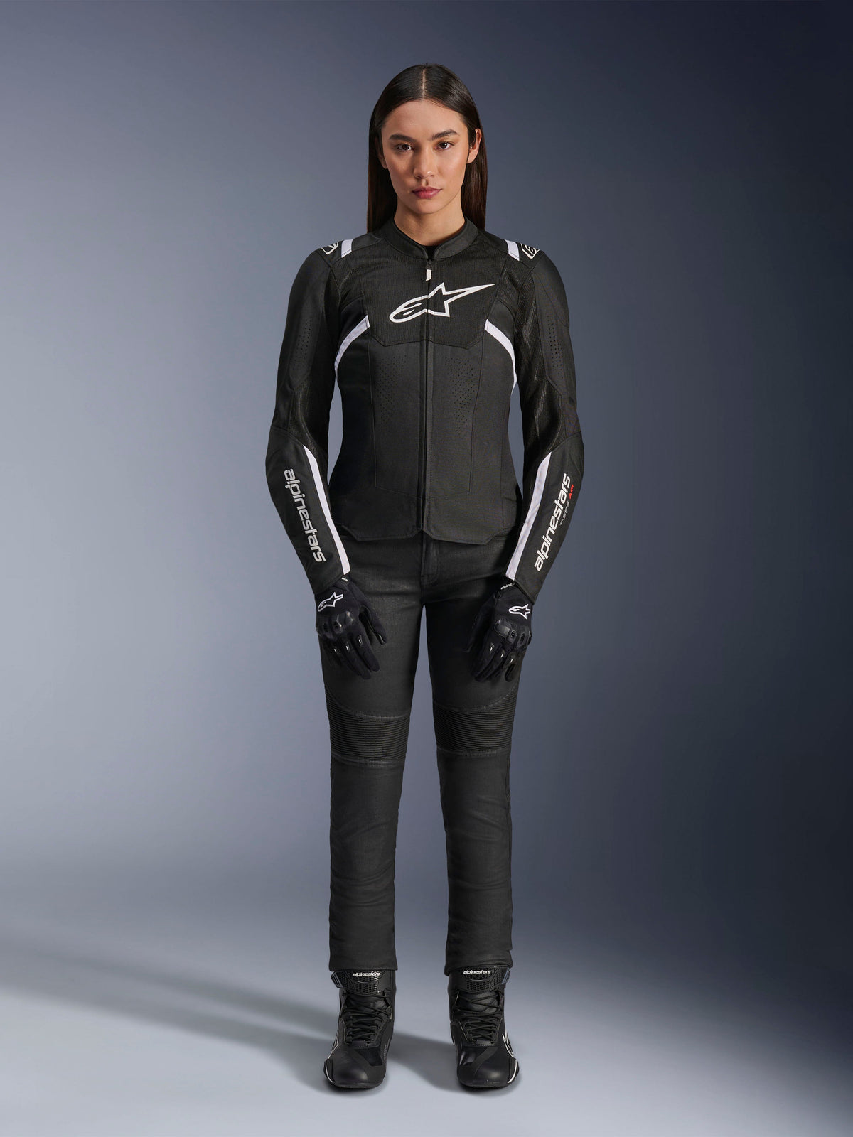 Alpinestars Stella T-Sps Air V2 Jas, motorjas voor dames, zwart en wit, voorzien van mesh-panelen en witte accenten, gedragen met zwarte broek, handschoenen en laarzen, sportieve pasvorm voor stedelijk rijden