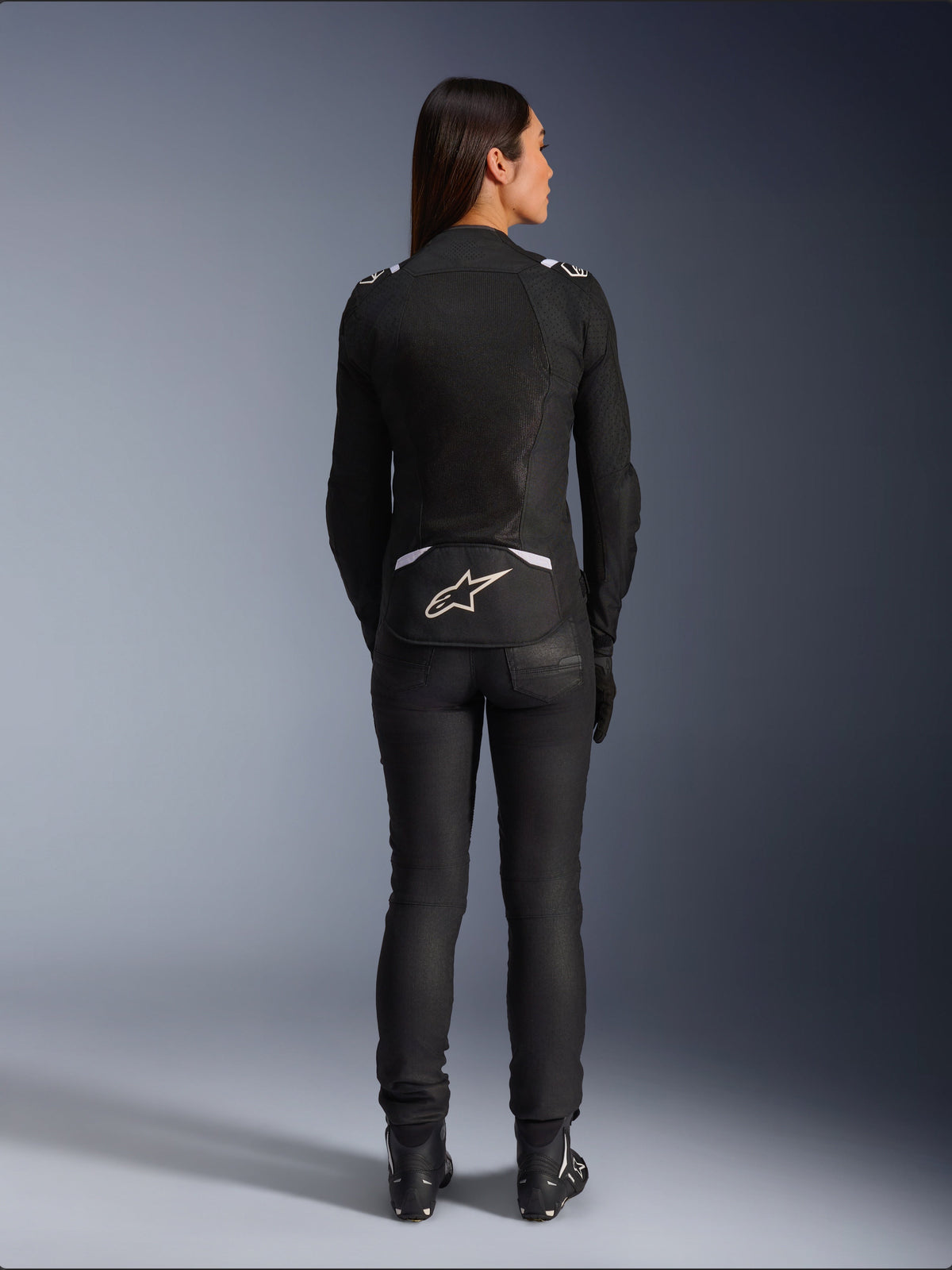 Alpinestars Stella T-SPS Air v2 Jas, motorjas voor dames, zwart en wit, achteraanzicht met mesh-ventilatiepanelen en wit logo op de onderrug, gedragen met zwarte motorbroek en laarzen, urban sportuitrusting