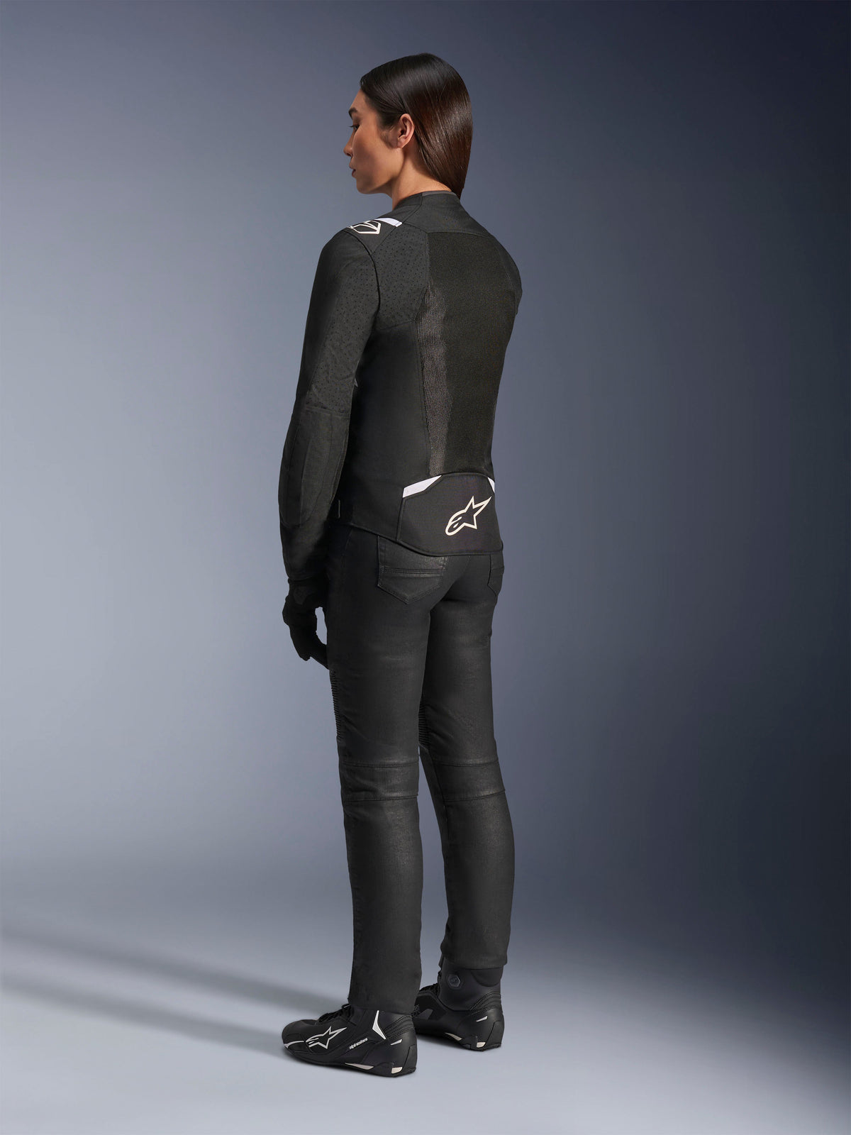 Alpinestars Stella T-Sps Air V2 Jas, zwart en wit, achteraanzicht met mesh-panelen en logo op de onderrug, zwarte motorbroek en motorschoenen, sportieve textiele weguitrusting voor dames