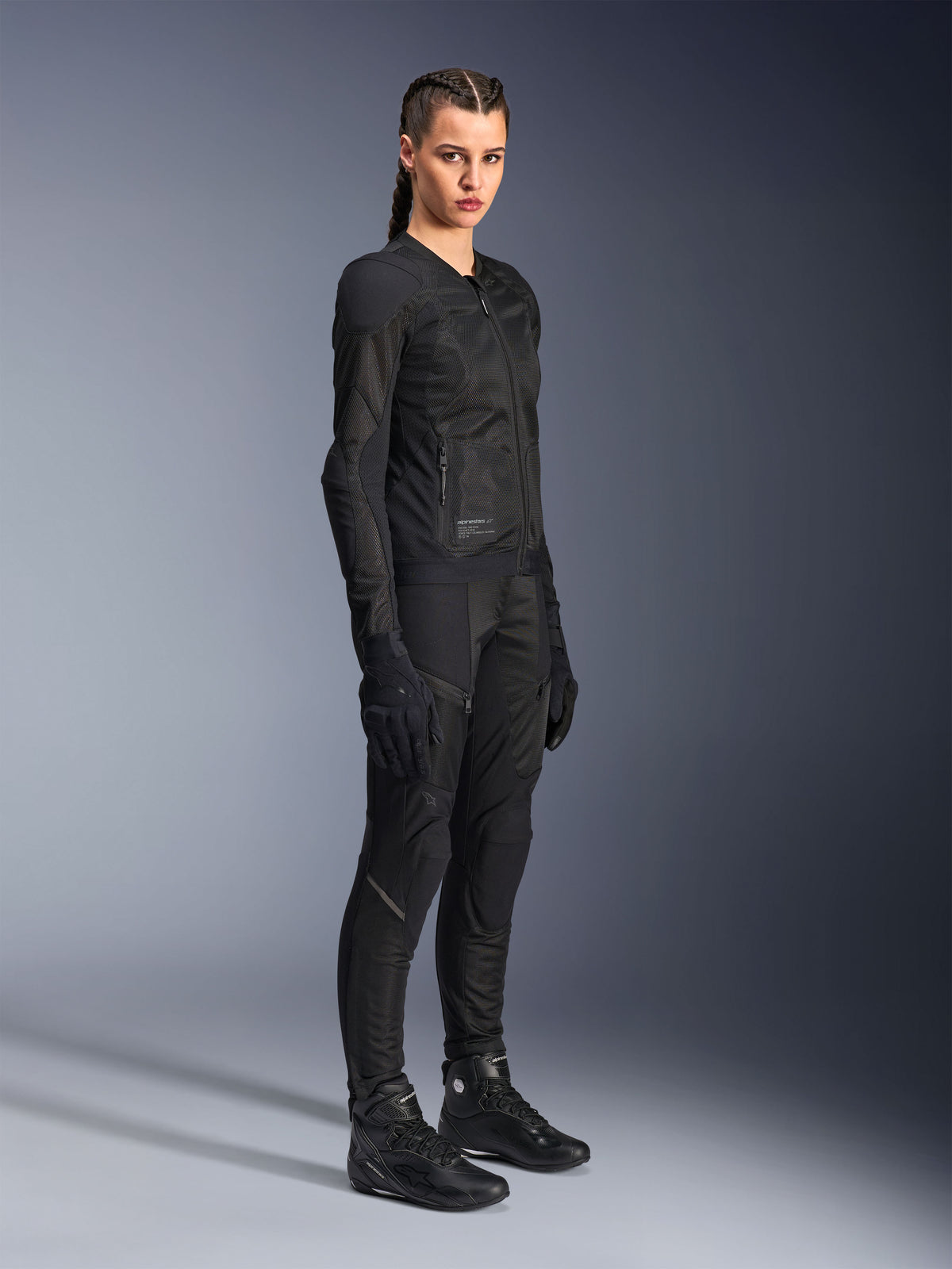 Motarde portant la veste Alpinestars Stella Troop-Air noire, dotée d'une construction technique en maille 2D, accompagnée d'un pantalon de moto, de gants et de bottes noirs assortis, conçue pour la conduite urbaine
