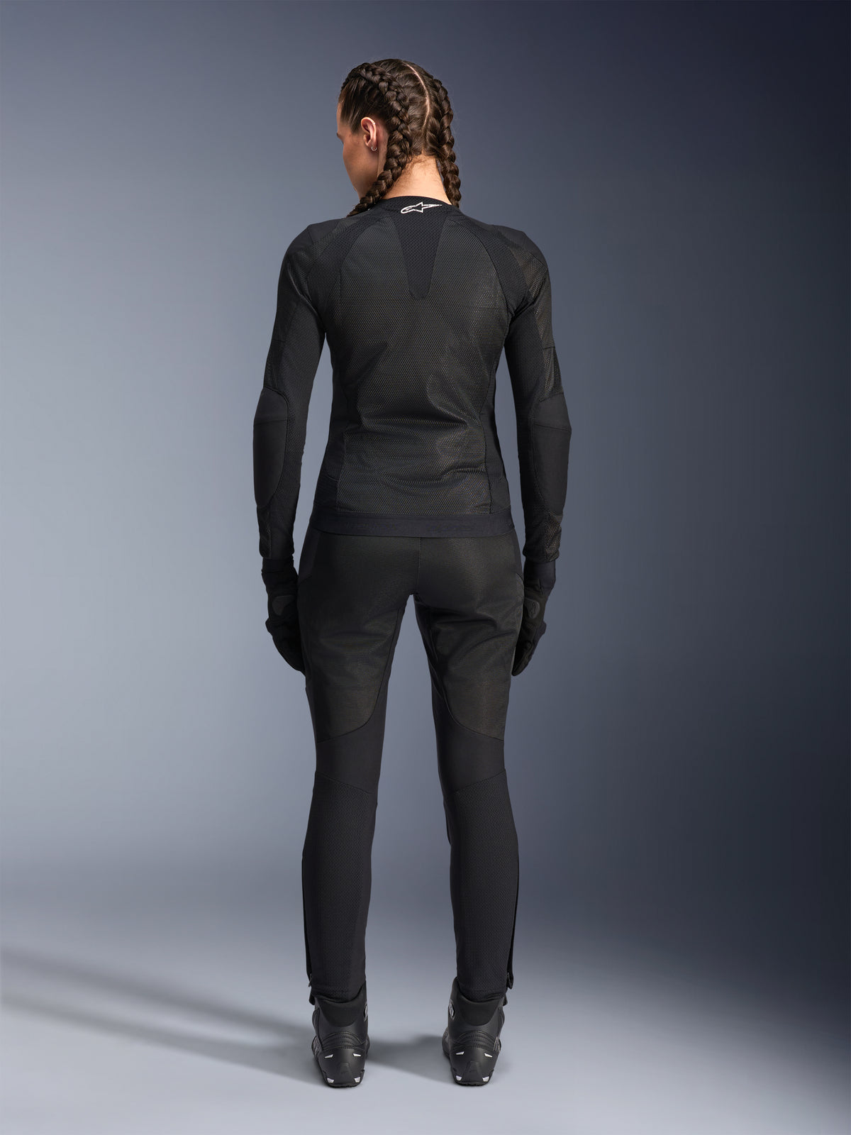 Veste Alpinestars Stella Troop-Air, veste de moto pour femme, noire, vue arrière d'une motarde portant une veste technique en maille, associée à un pantalon de moto, des gants et des bottes noirs assortis, coupe ajustée et respirante avec un logo Alpinestars blanc sur le col