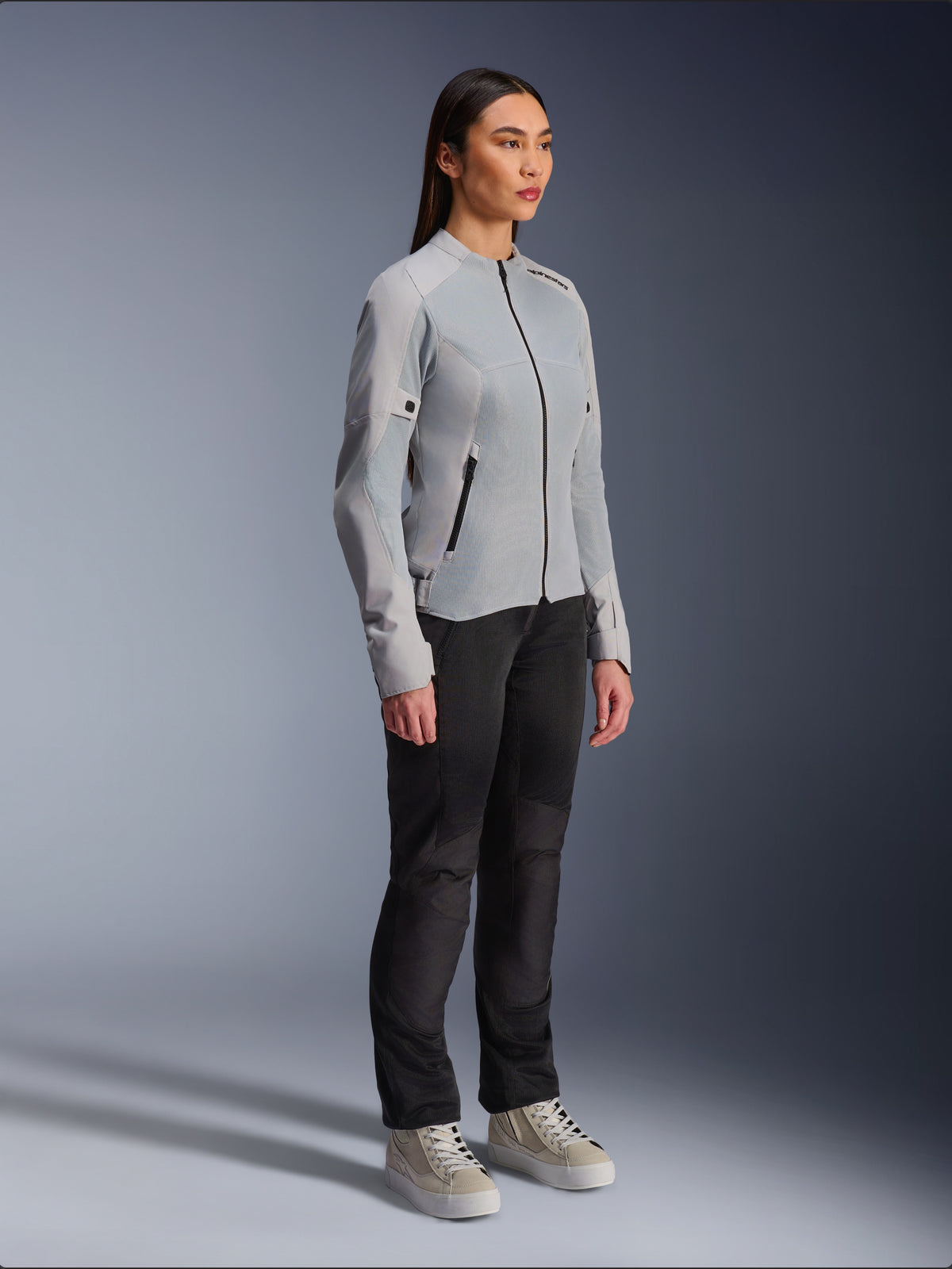 Woman wearing the Alpinestars Stella C-1 Air Jacket in Silver, lightweight textile and mesh motorcycle jacket, styled with black riding pants and casual sneakers, clean urban riding aesthetic.