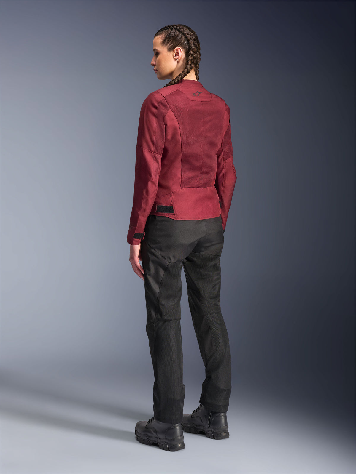 Veste pour femme Alpinestars Stella C-1 Air, Burgundy, vue de dos montrant les panneaux en maille et les détails raffinés, portée avec un pantalon de moto et des bottes noirs, équipement de moto urbain contemporain.