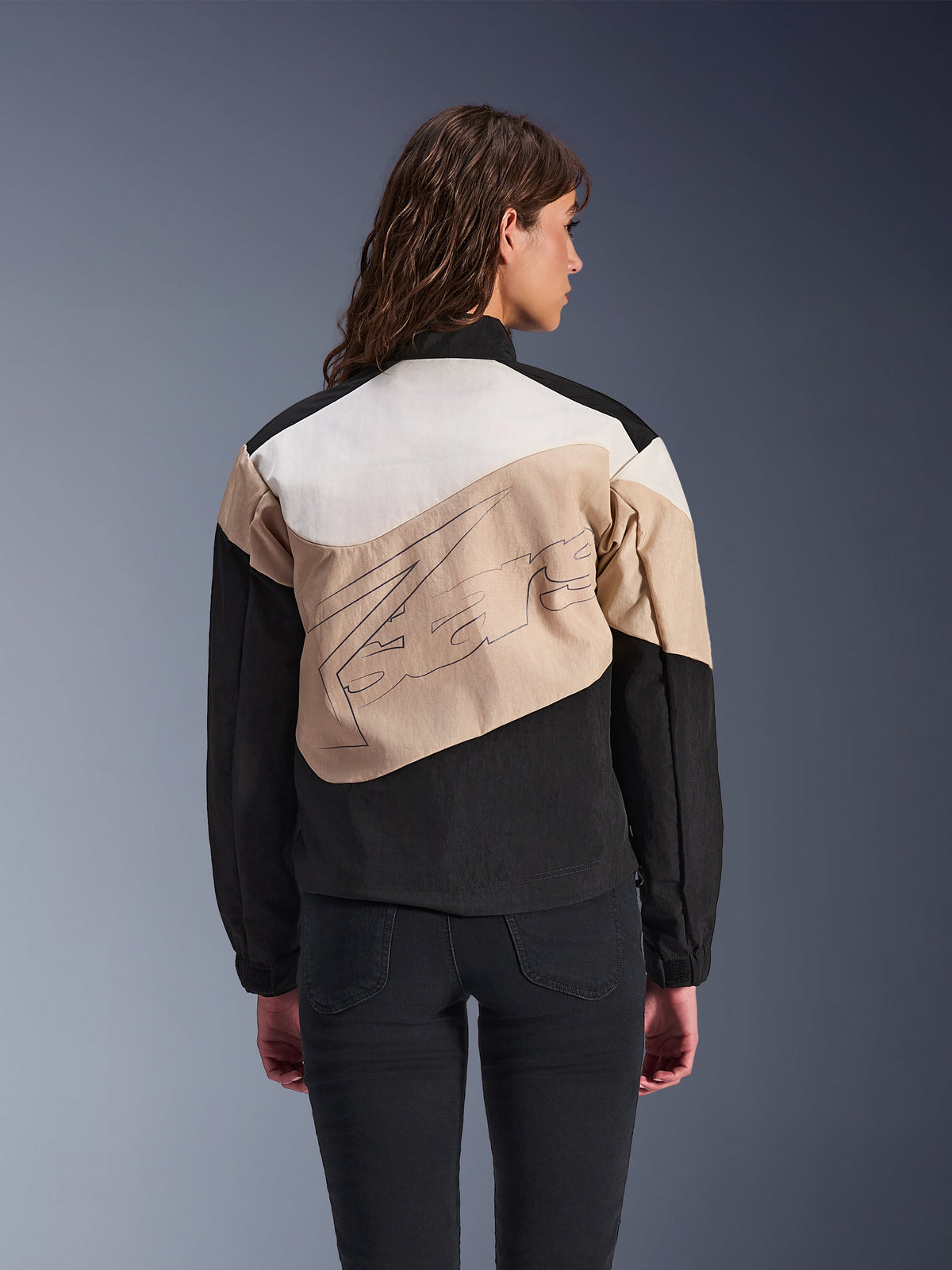 Alpinestars Stella Moshell Jacket, urban motorjas voor dames, zwart, zand en off-white, achteraanzicht op een model, asymmetrisch color-block ontwerp met grote grafische print op de rug, moderne op streetwear geïnspireerde beschermende motorkleding