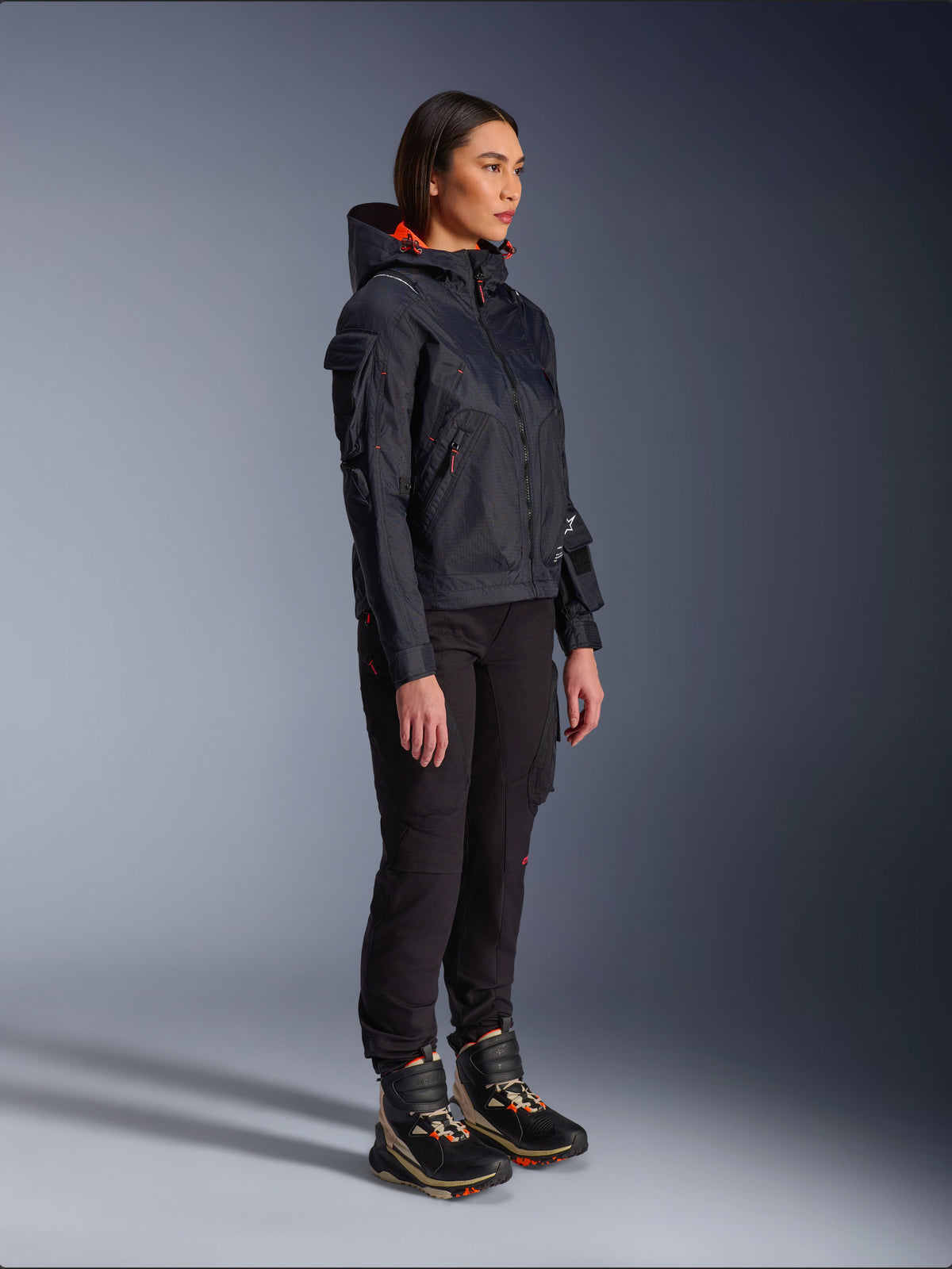 Alpinestars Actea damesbroek in het zwart, regular fit met cargozakken, gecombineerd met een zwart Molly Air Jacket met oranje accenten en hoge motorschoenen, eigentijdse urban motorkleding voor dames