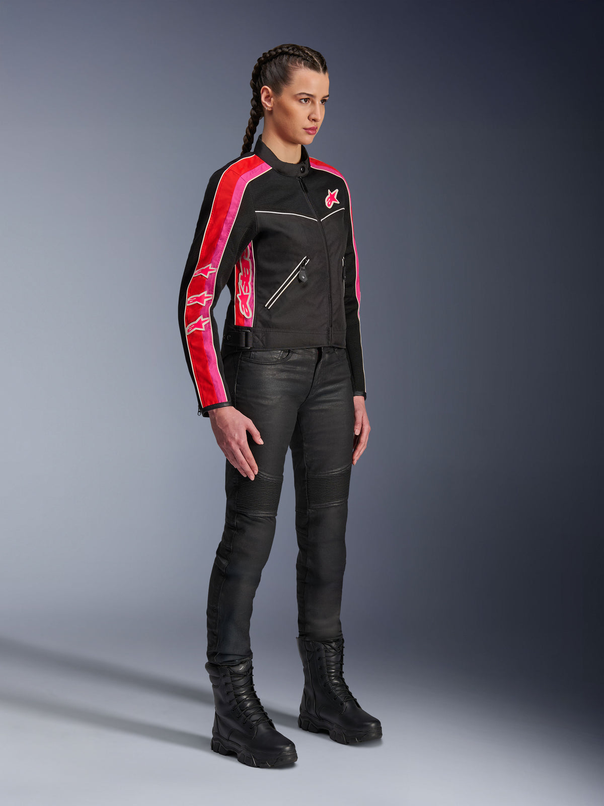 Alpinestars Stella T-Dyno Air Jacke, Damen-Motorradjacke, Schwarz mit leuchtend roten und fuchsiafarbenen Streifen an den Ärmeln, getragen mit schwarzer Motorradhose und Stiefeln, Vintage-inspiriertes Mesh-Design für urbanes Fahren