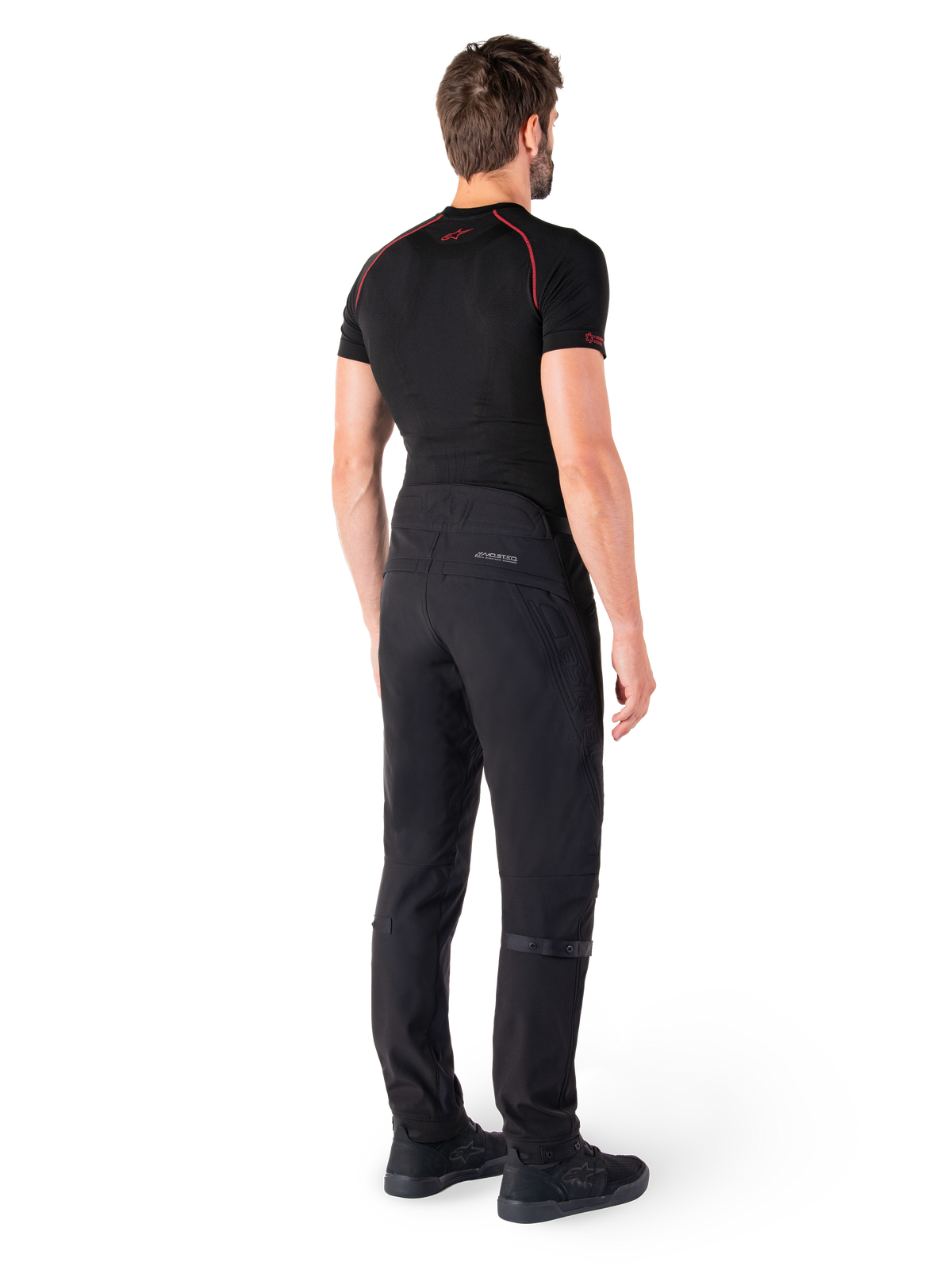 Alpinestars Alden Hose, Schwarz, urbane Motorradhose von hinten an einem Model gezeigt, getragen mit einem schwarzen kurzärmeligen Baselayer und schwarzen Motorradschuhen, mit gesteppten Details und reflektierendem MO.ST.EQ. Branding auf der Rückenpasse.