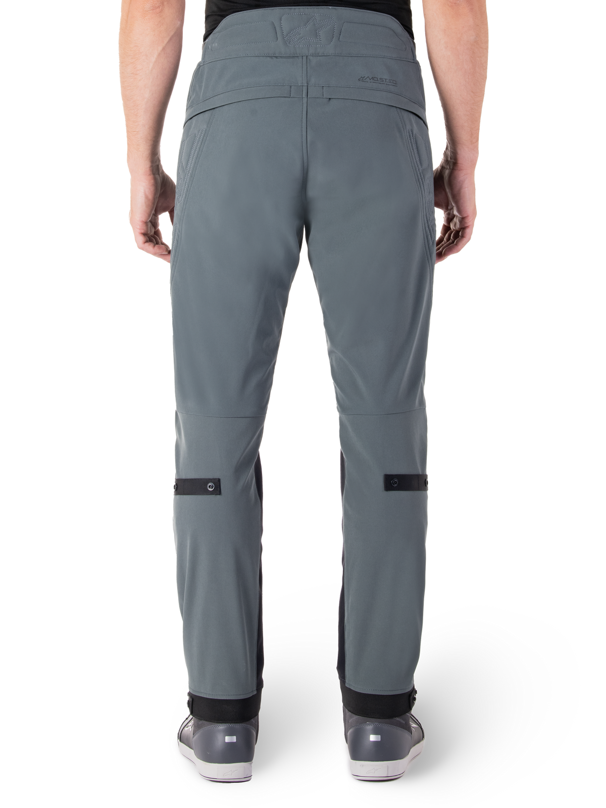 Alpinestars Alden Hose, Urban Gray, Rückansicht einer urbanen Motorradhose für Herren, schmale Passform unterhalb des Knies mit schwarzen Wadenverstellriemen, hoher Bund mit MO.ST.EQ. Wortmarke auf der Rückenpasse, getragen mit grauen Reitschuhen