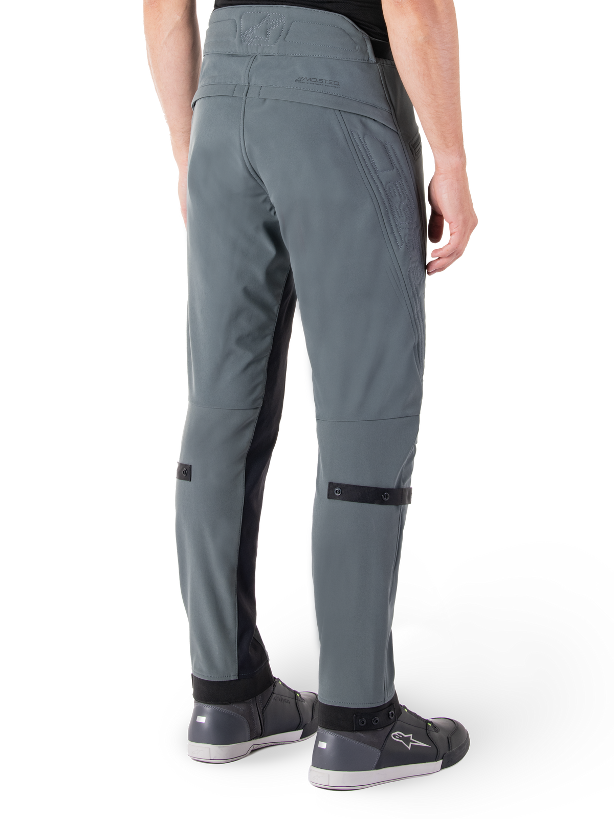 Alpinestars Alden Hose, Urban Grau, seitliche Rückansicht, Streetwear-inspirierte technische Motorradhose mit gesteppten Details an der Taille und schwarzen Wadenriemen, kombiniert mit grauen Motorradschuhen, moderne urbane Motorradausrüstung