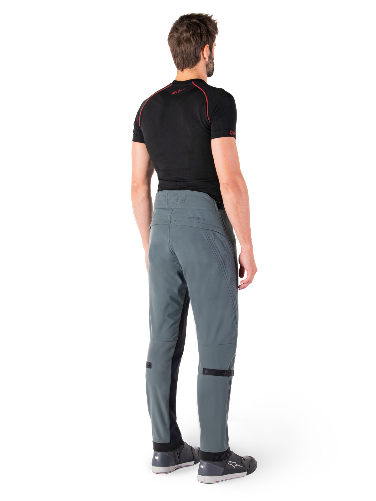 Alpinestars Alden Hose, Urban Grau, Rückansicht, technische Textil-Motorradhose mit gesteppten Details am oberen hinteren Bund und an den Beinen, kombiniert mit einem schwarzen Baselayer und grauen Motorradschuhen, moderner urbaner Streetwear-Stil.