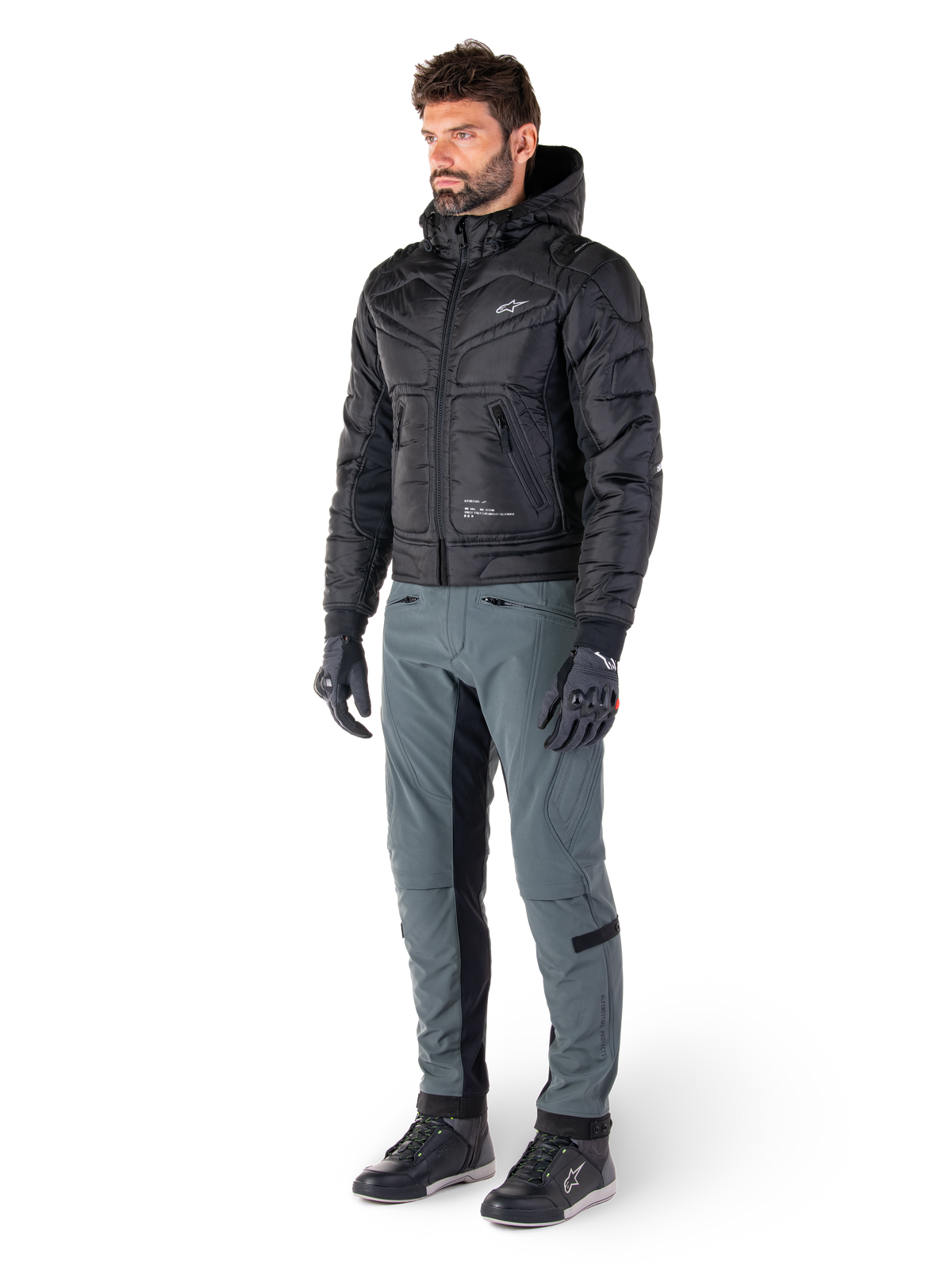 Alpinestars Alden Hose in Urban Gray, getragen von einem Model mit einer schwarzen gesteppten Kapuzenjacke, Handschuhen und Motorradschuhen, mit gesteppten Details an den Seiten und schwarzen Einsätzen an den Beininnenseiten, Streetwear-inspirierte urbane Motorradausrüstung