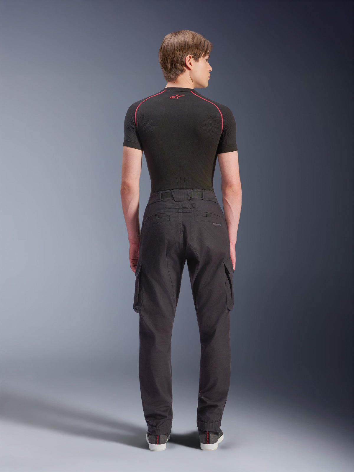 Alpinestars Flex-AST Cargo Pants - Short, zwarte stedelijke motorbroek van achteren gezien, met cargozakken aan de zijkant en elastische zomen, gedragen met een zwarte basislaag met korte mouwen en rode contraststiksels