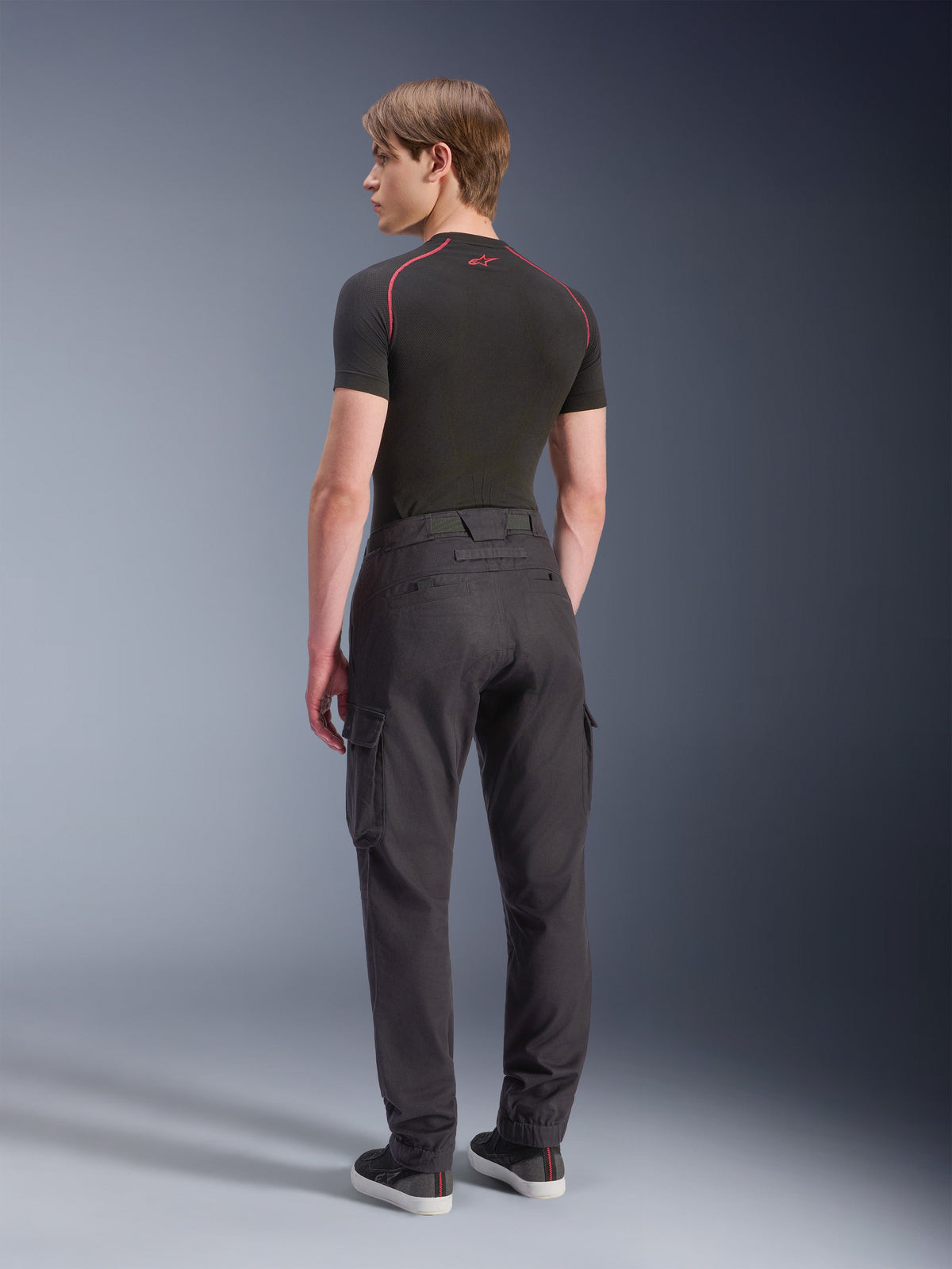Alpinestars Flex-AST Cargo Broek - Kort, motorcargobroek, zwart, achteraanzicht van model dat een regular tapered cargobroek draagt met zijzakken en elastische zomen, gecombineerd met een zwarte basislaag en vrijetijdsschoenen