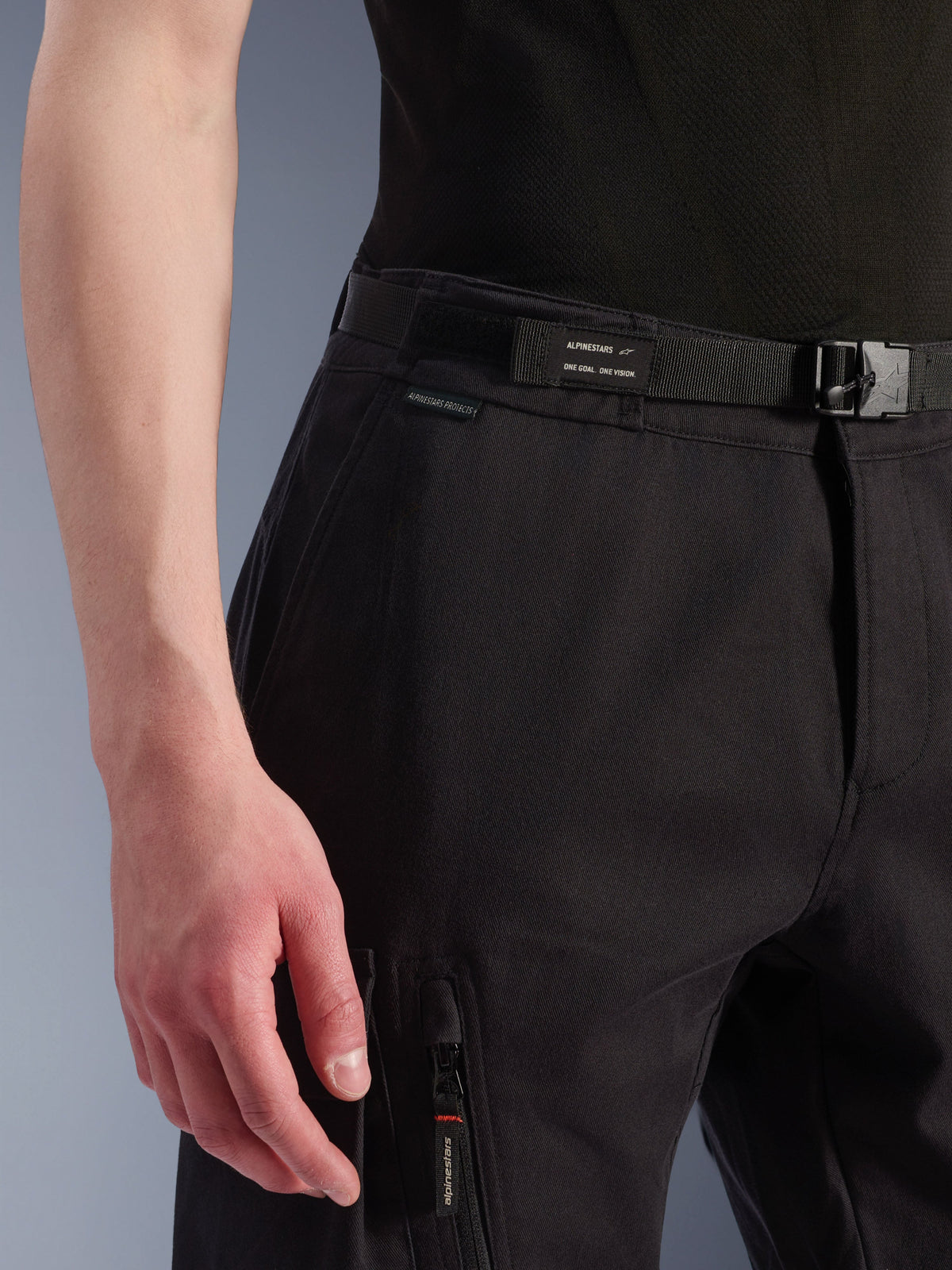 Alpinestars Flex-AST Cargo broek, urban motorbroek, zwart, detailopname van taille en zijzak, met een geïntegreerde riem met Alpinestars-branding, gespsluiting en een ritszak met een merk-ritstrekker, technische textielconstructie voor stedelijk rijden.