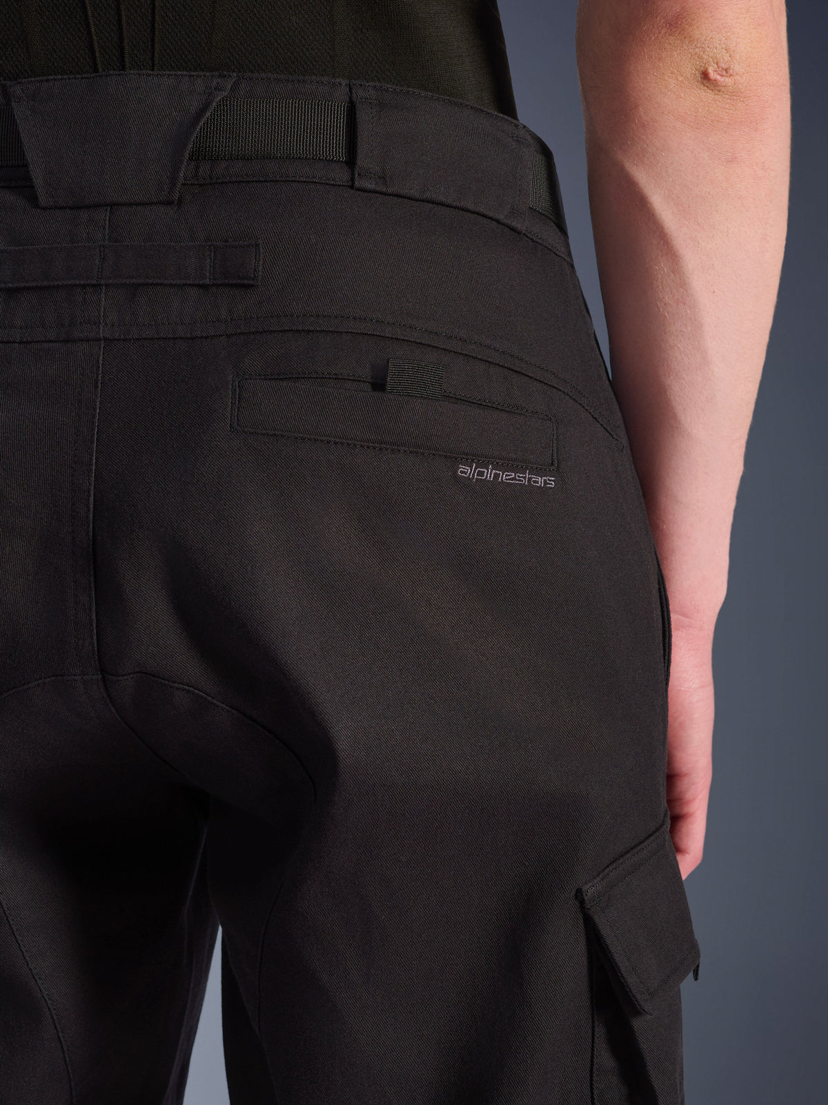 Alpinestars Flex-AST Cargo Broek in het zwart, urban motorbroek, close-up van de achterzijde met gedetailleerde achterzak, subtiele branding, grote riemlussen en een cargozak aan de zijkant, vervaardigd uit duurzaam stretchtextiel
