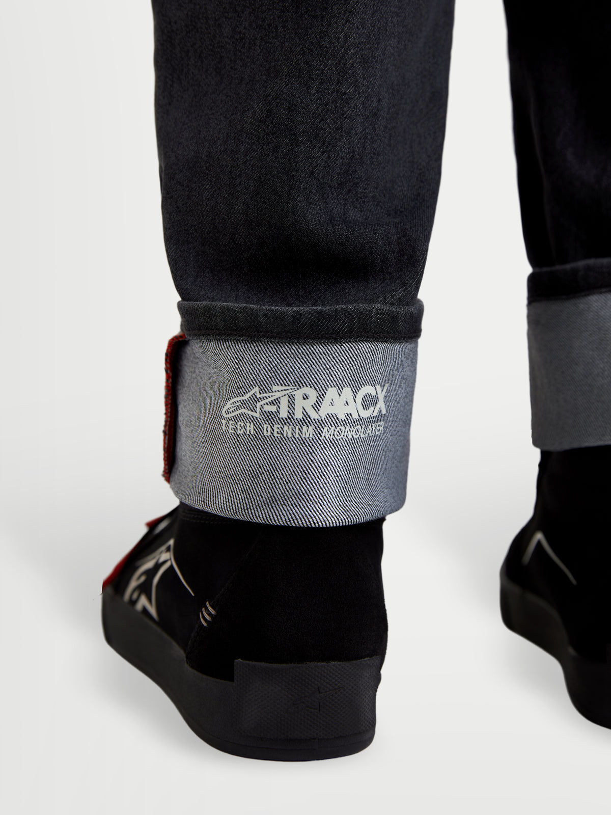 Alpinestars Flex Ast 7 Denim Pantalons, pantalon de moto en denim noir délavé, vue rapprochée de l'ourlet à revers affichant le marquage technique A-TRAACX et les détails de lisière