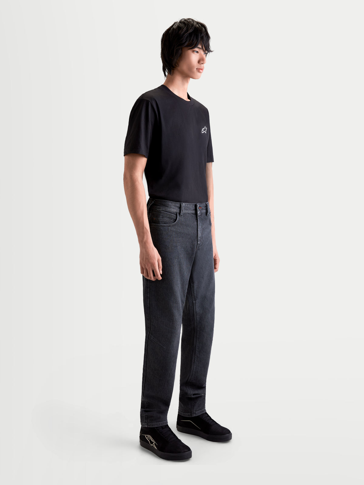 Alpinestars Flex Ast 7 Denim Pantalons, pantalon de moto urbain contemporain pour homme en noir délavé, vue de profil sur un modèle portant un t-shirt noir et des chaussures, construction en denim technique monocouche certifié AA