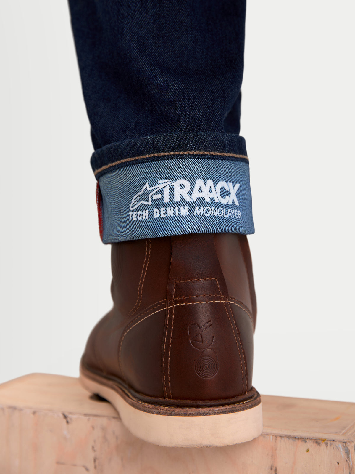 Alpinestars Flex Ast 7 Denim broek, urban motorjeans voor heren, donkerblauw, detailopname van de omgeslagen zoom met A-TRAACX technical denim branding en bruine leren laarzen