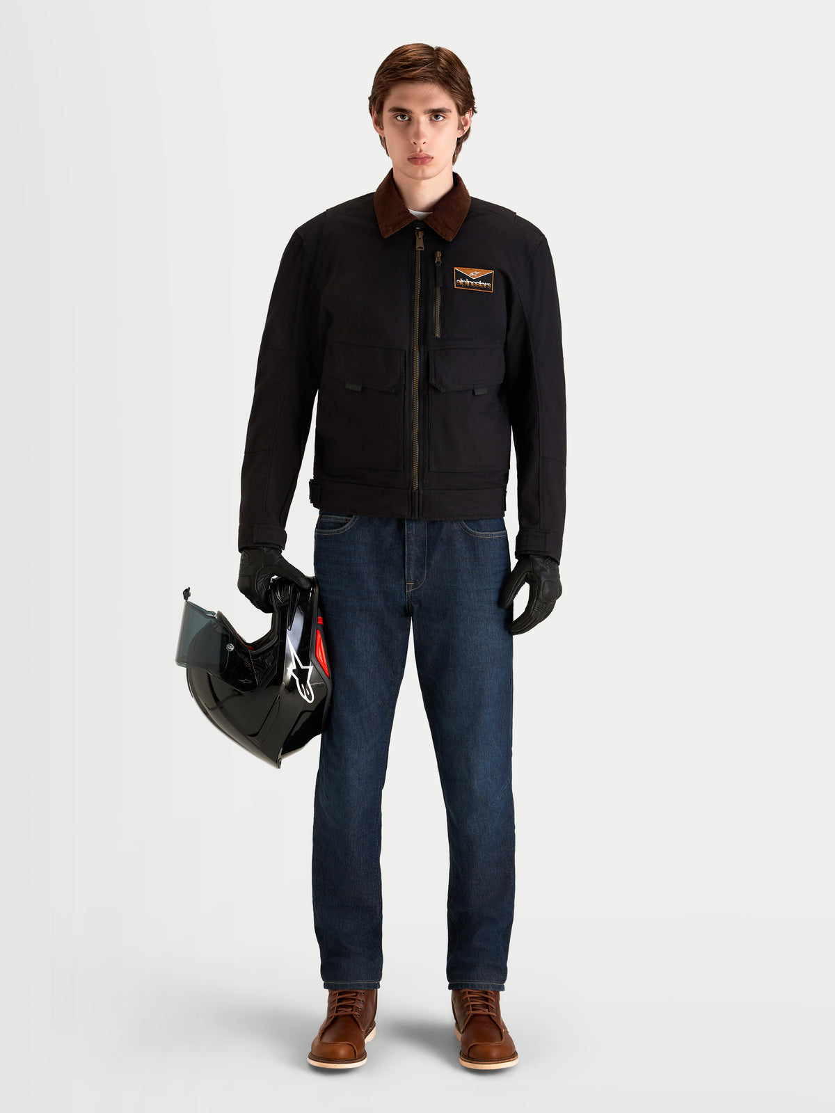 Alpinestars Flex Ast 7 Denim Broek, urban motorjeans voor heren in donkerblauw, gedragen door een model met een zwarte jas met bruine kraag en helm in de hand