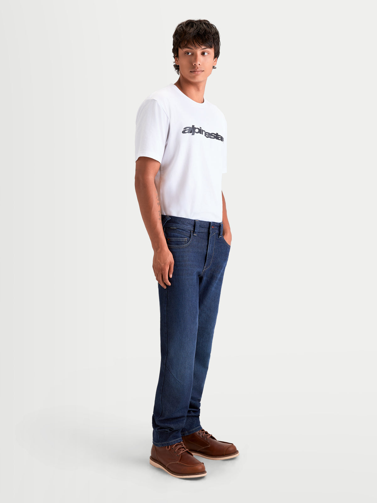 Alpinestars Flex Ast 7 Denim Broek, heren urban motorjeans in donkerblauw, zijprofiel op model met wit t-shirt en bruine laarzen, met AA-gecertificeerde CORDURA constructie