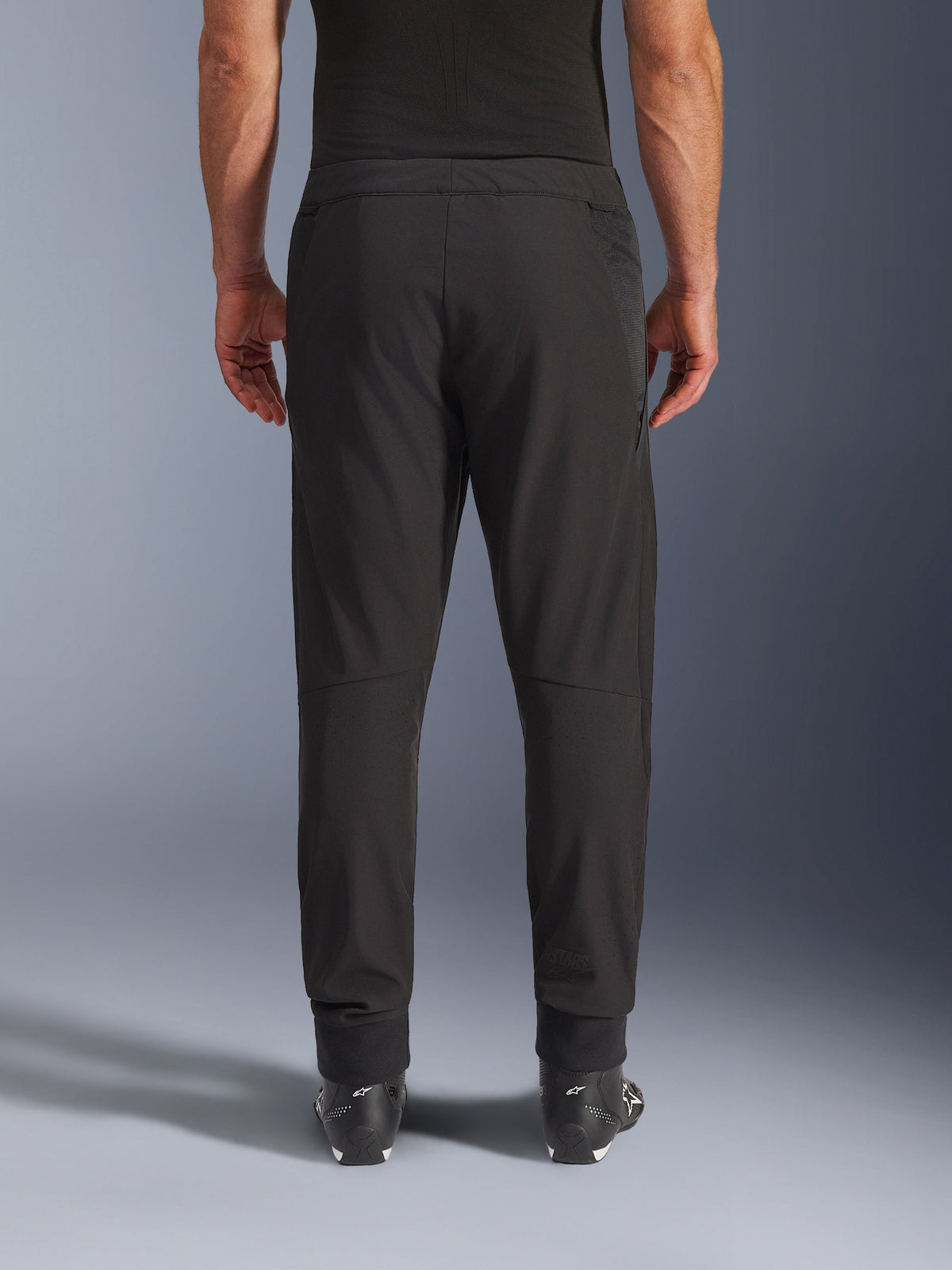 Alpinestars Aeroshell Airflow Hose, Schwarz, Rückansicht, mit laserperforierten Zonen an den Waden und Mesh-Einsätzen, kombiniert mit schwarzen Alpinestars-Stiefeln, leichtes Softshell-Design für Sport und Touring
