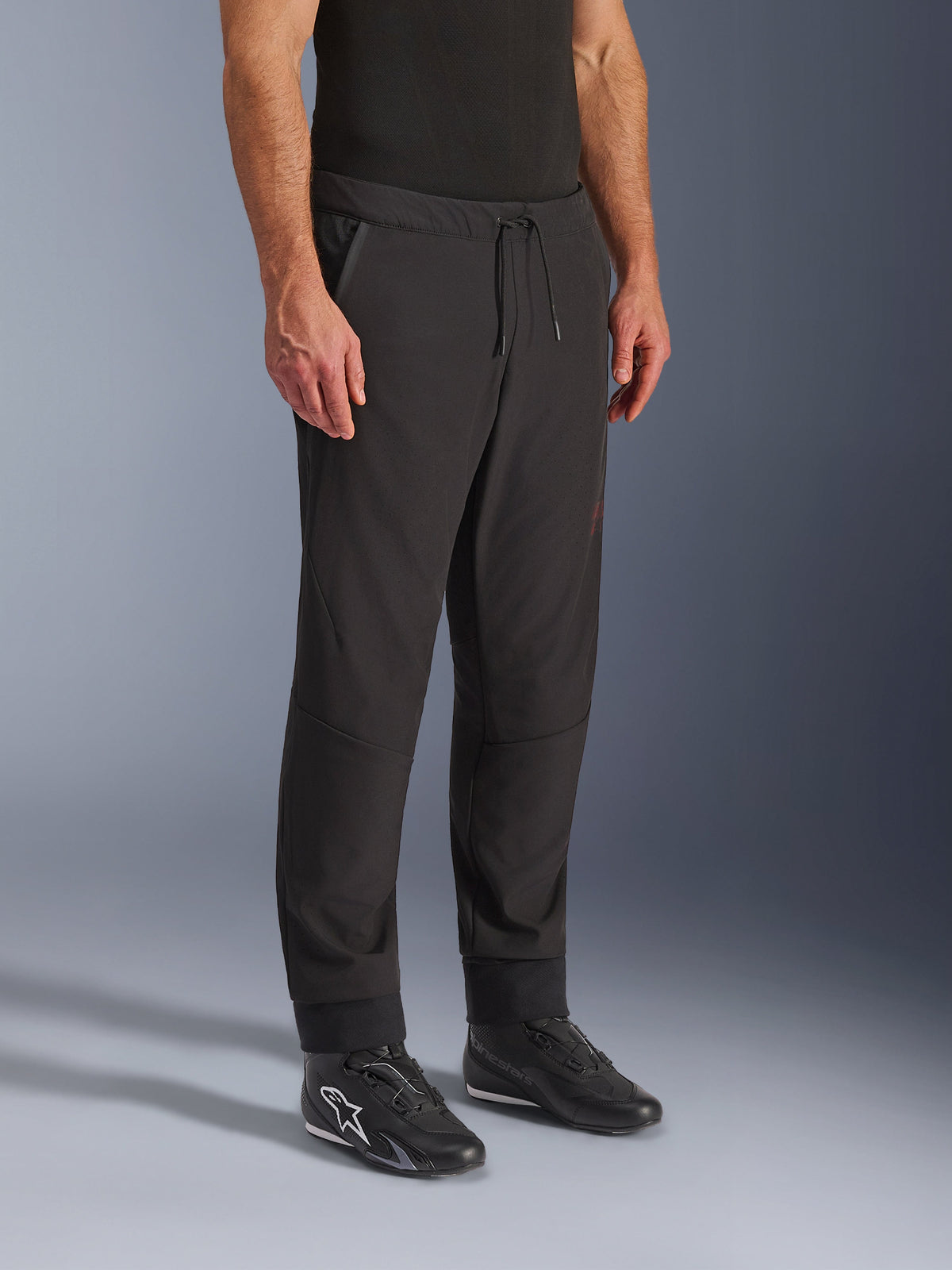 Alpinestars Aeroshell Airflow Hose, schwarze Motorradhose, getragen von einem Modell mit schwarzen Fahrschuhen, mit Kordelzug am Bund, Knöchelbündchen und laserperforiertem Softshell-Gewebe für maximale Belüftung