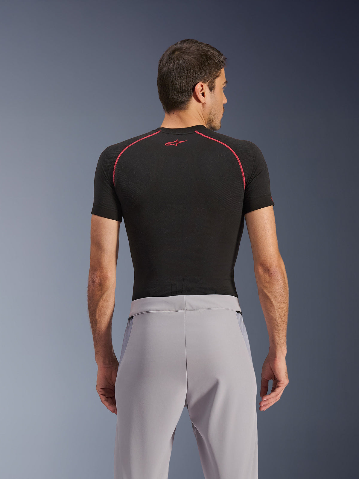 Pantalon Alpinestars Aeroshell Airflow, Gris Moyen, vue de dos, porté avec un vêtement de corps noir à manches courtes avec coutures et logo rouges, doté d'un textile softshell extensible léger et de panneaux en maille pour une ventilation maximale, coupe sport ergonomique pour la conduite à moto