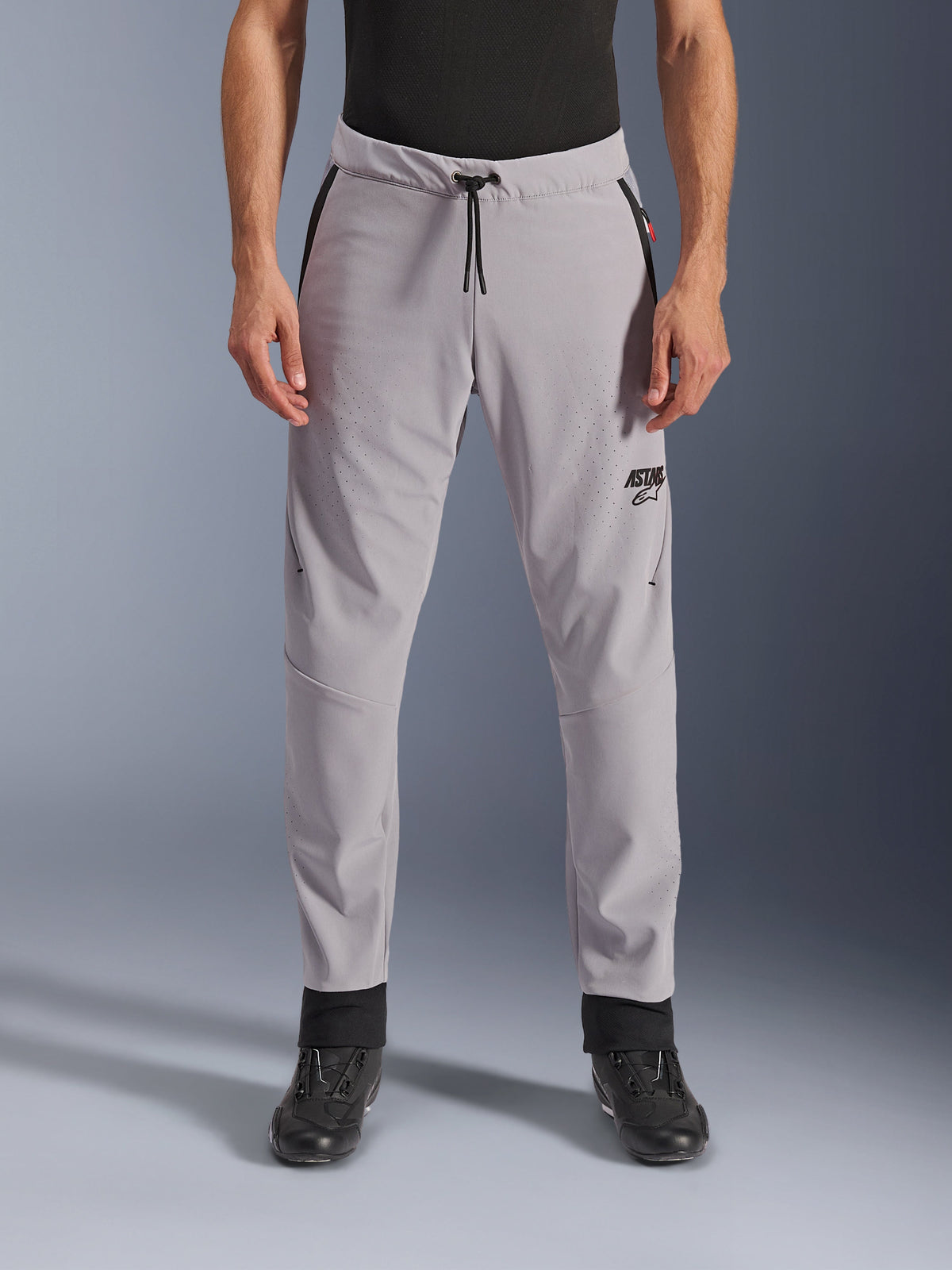 Pantalon Alpinestars Aeroshell Airflow, Gris Moyen, vue de face montrant les zones perforées au laser sur les cuisses et les tibias, taille à cordon de serrage noir et logo ASTARS noir, châssis en softshell léger pour la conduite par temps chaud