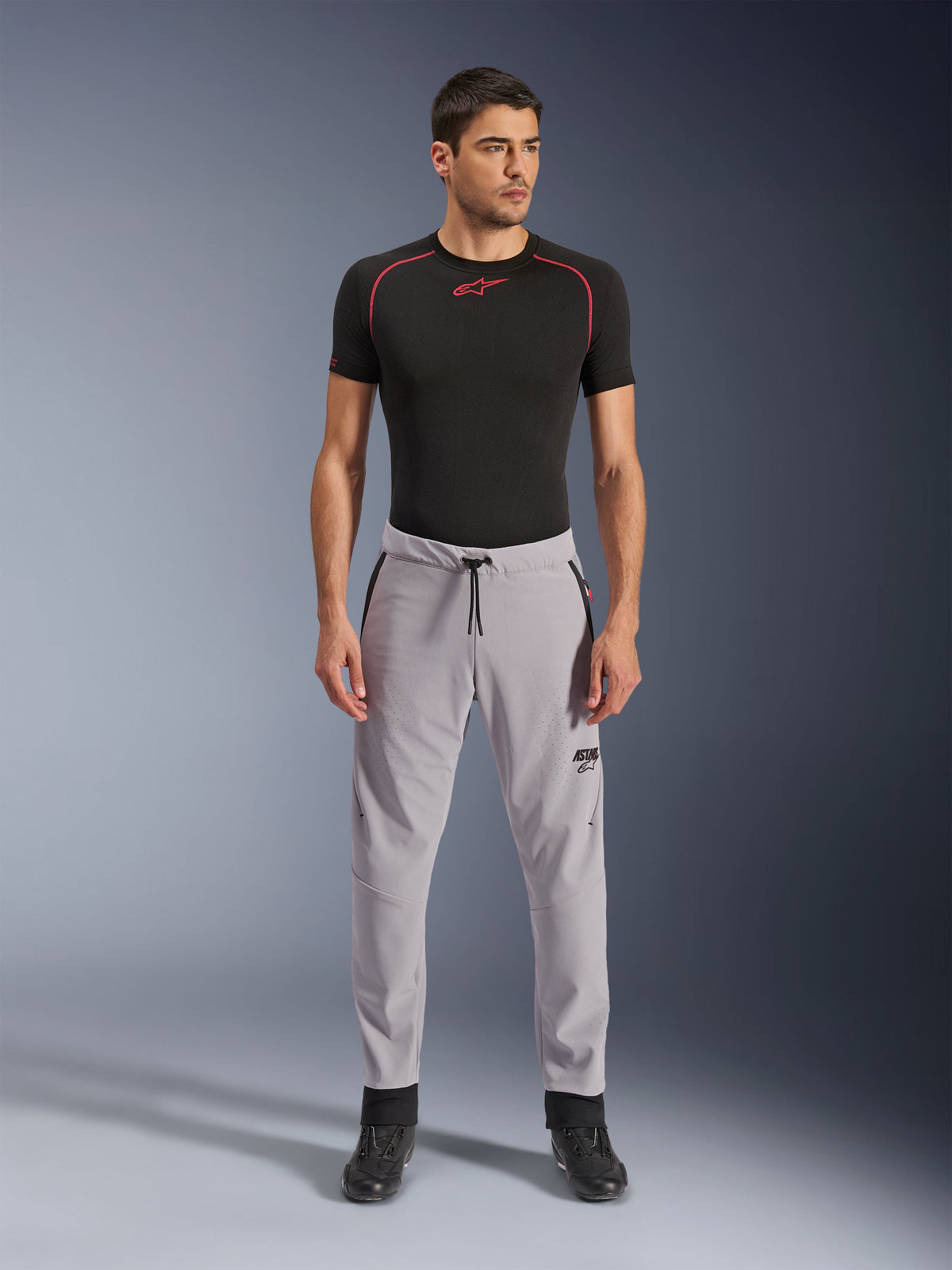 Pantalon Alpinestars Aeroshell Airflow, gris moyen, pantalon textile léger avec zones de ventilation perforées au laser et taille à cordon de serrage, porté par un mannequin avec un haut de compression noir et des bottes de moto noires, design de conduite sportive épuré et moderne