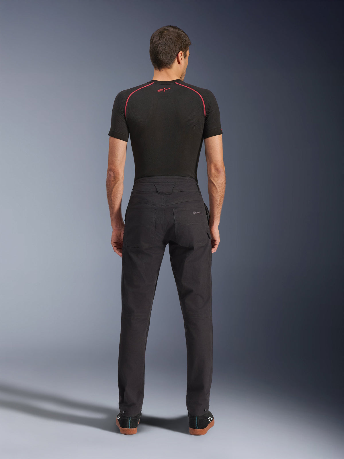 Alpinestars Flex-AST Canvas Pants, pantalon de moto urbain, noir, vue arrière montrant un design inspiré du style workwear avec poches arrière et taille arrière montante, porté avec une couche de base noire et des baskets, coupe ergonomique pour la conduite